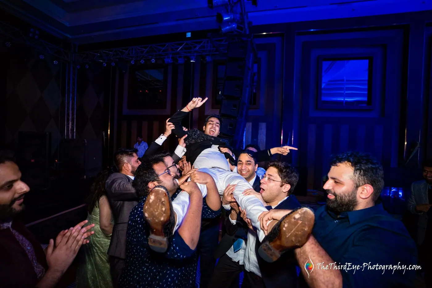 Friends hoist a man across their arms above the dance floor as others cheer and clap