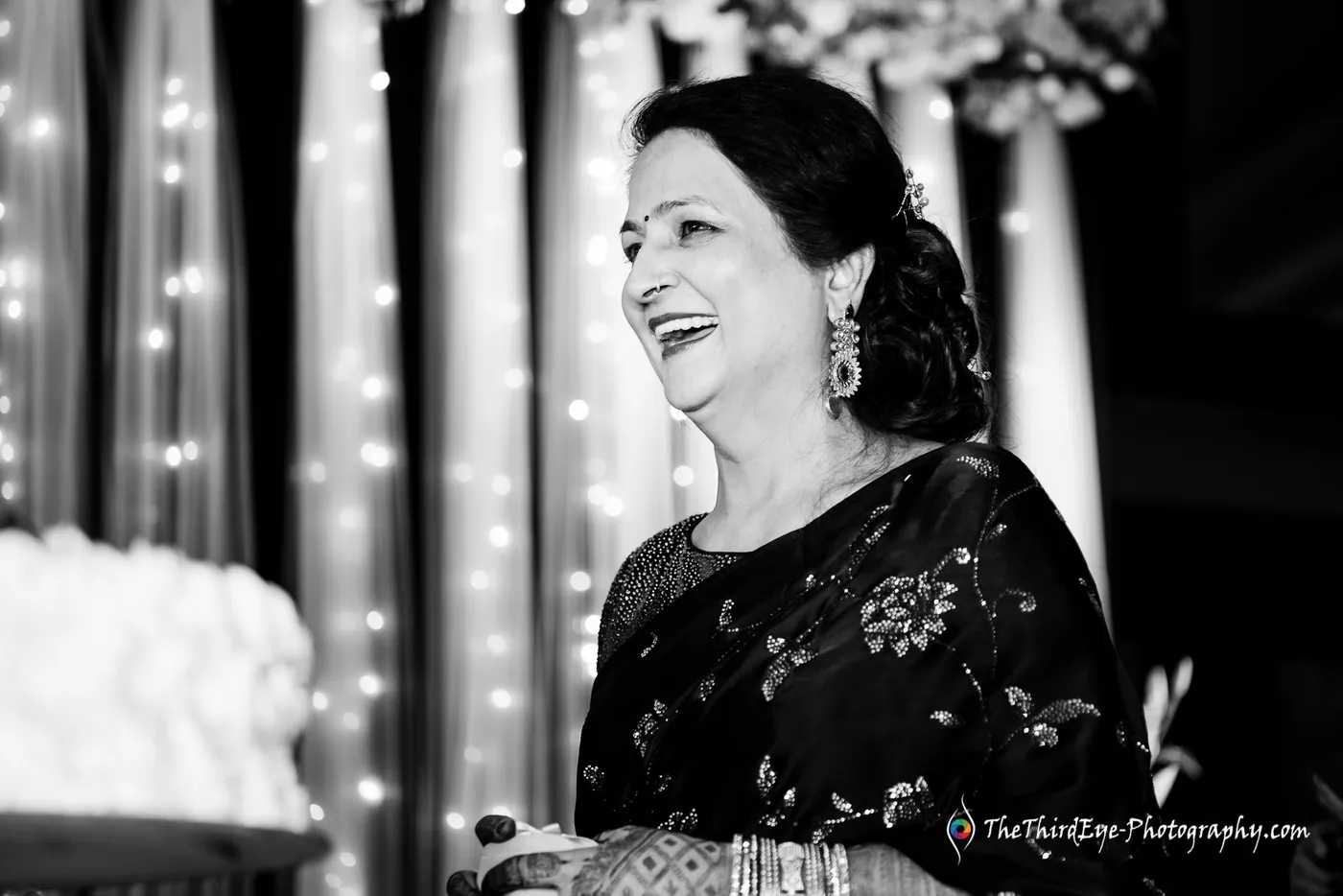 Black and white frame of a woman in a dark embroidered outfit laughing with her head thrown back