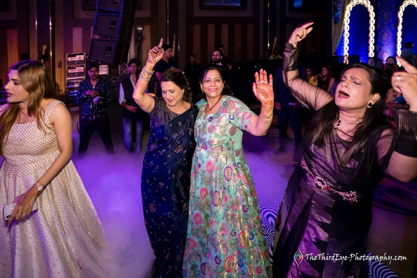 Women in gowns dance with arms raised through purple floor fog