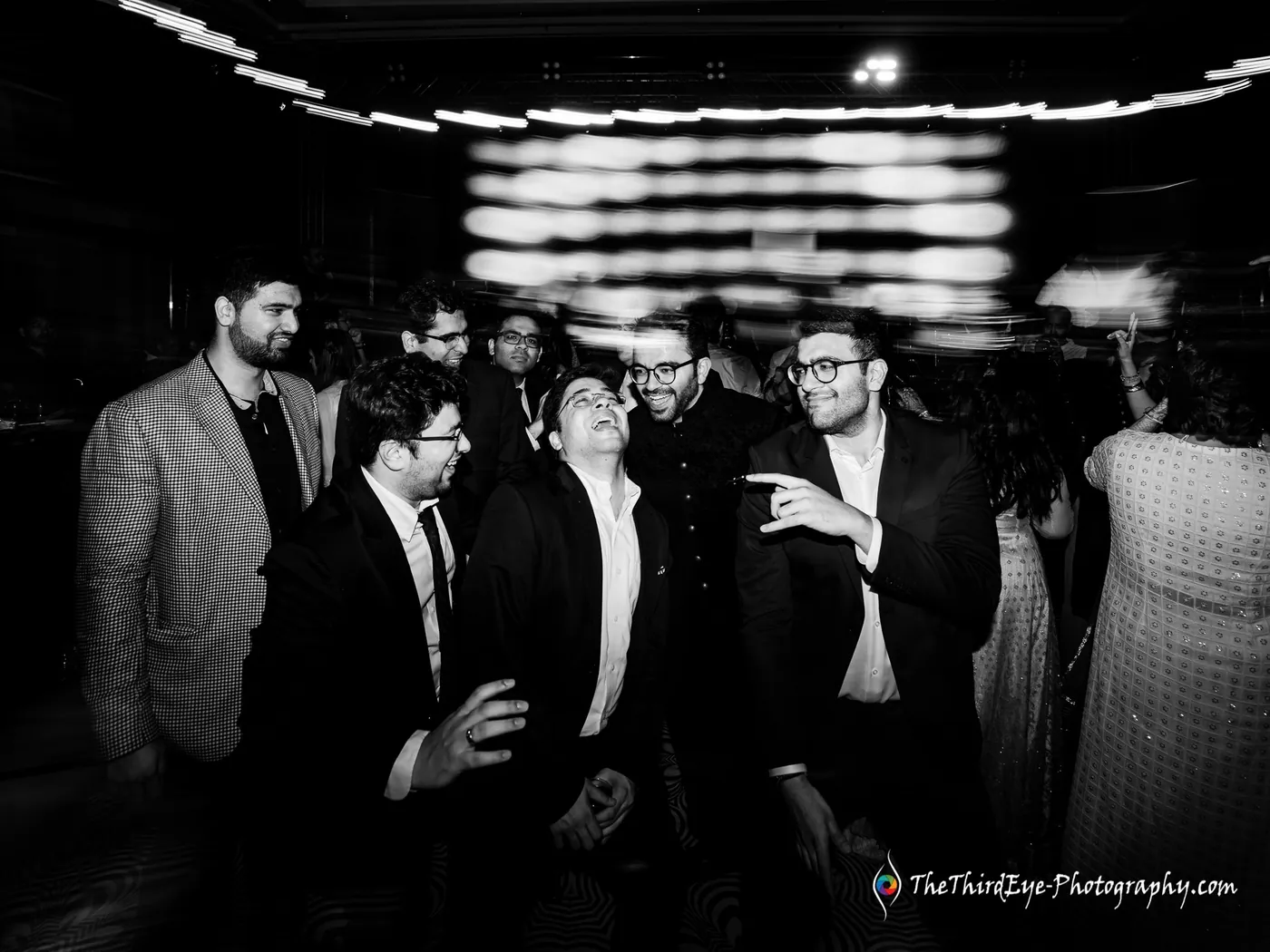 Black and white frame of a tight pack of men in dark jackets dancing and laughing together