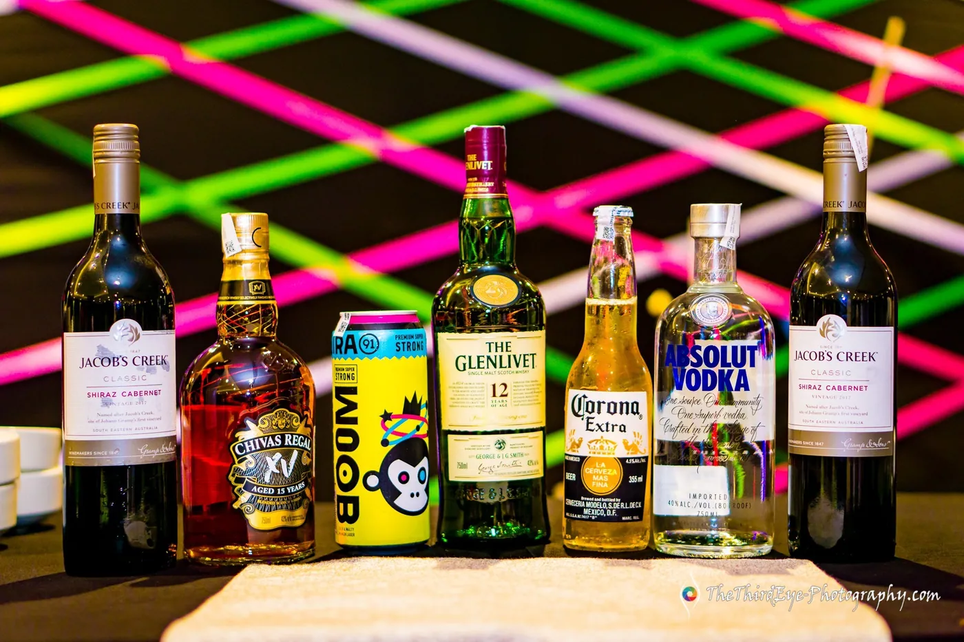 Bottles of whisky, wine, beer and vodka on a table with bright fluorescent laser lines glowing behind