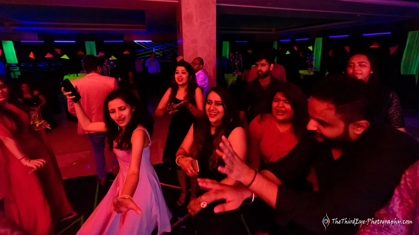 Guests crowd the dance floor in warm red light, a woman in pink swaying at the center