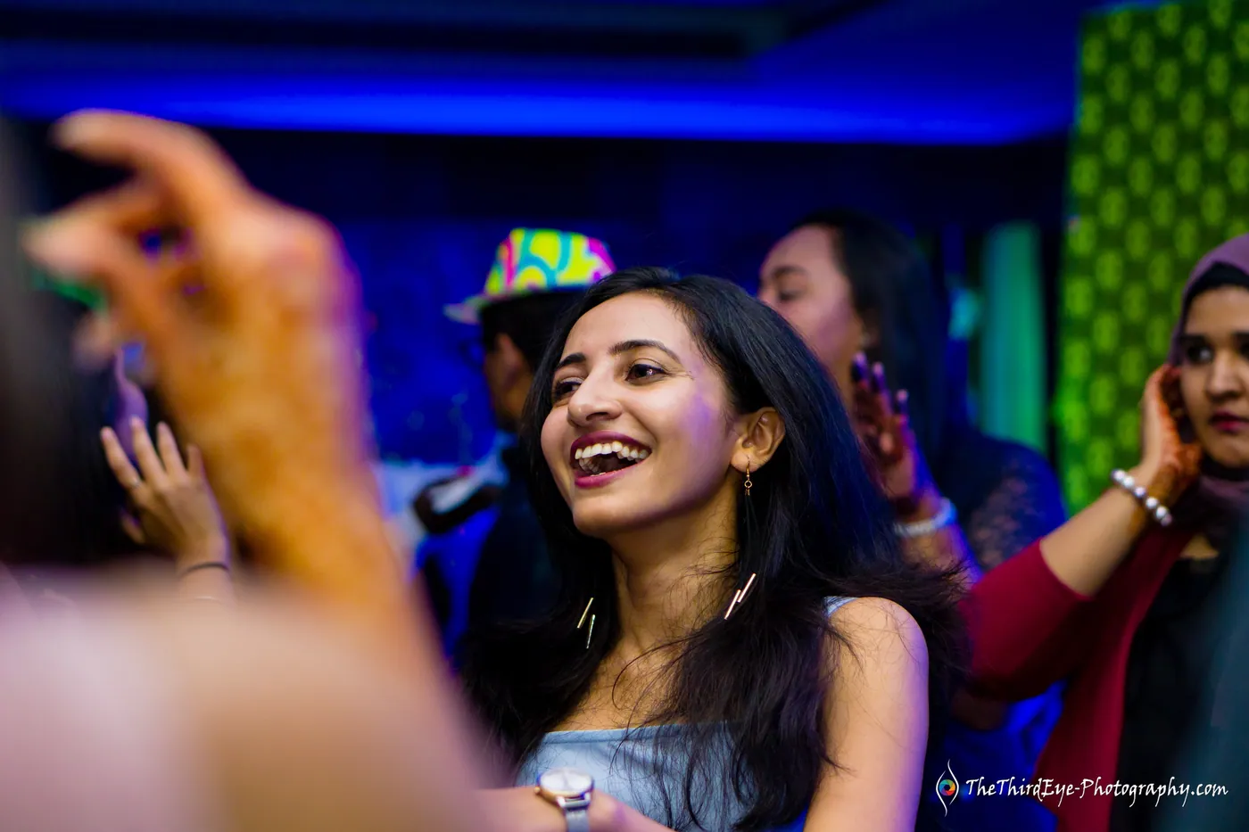 A woman laughs with her head tipped back in blue light as a blurred hand waves close to the lens