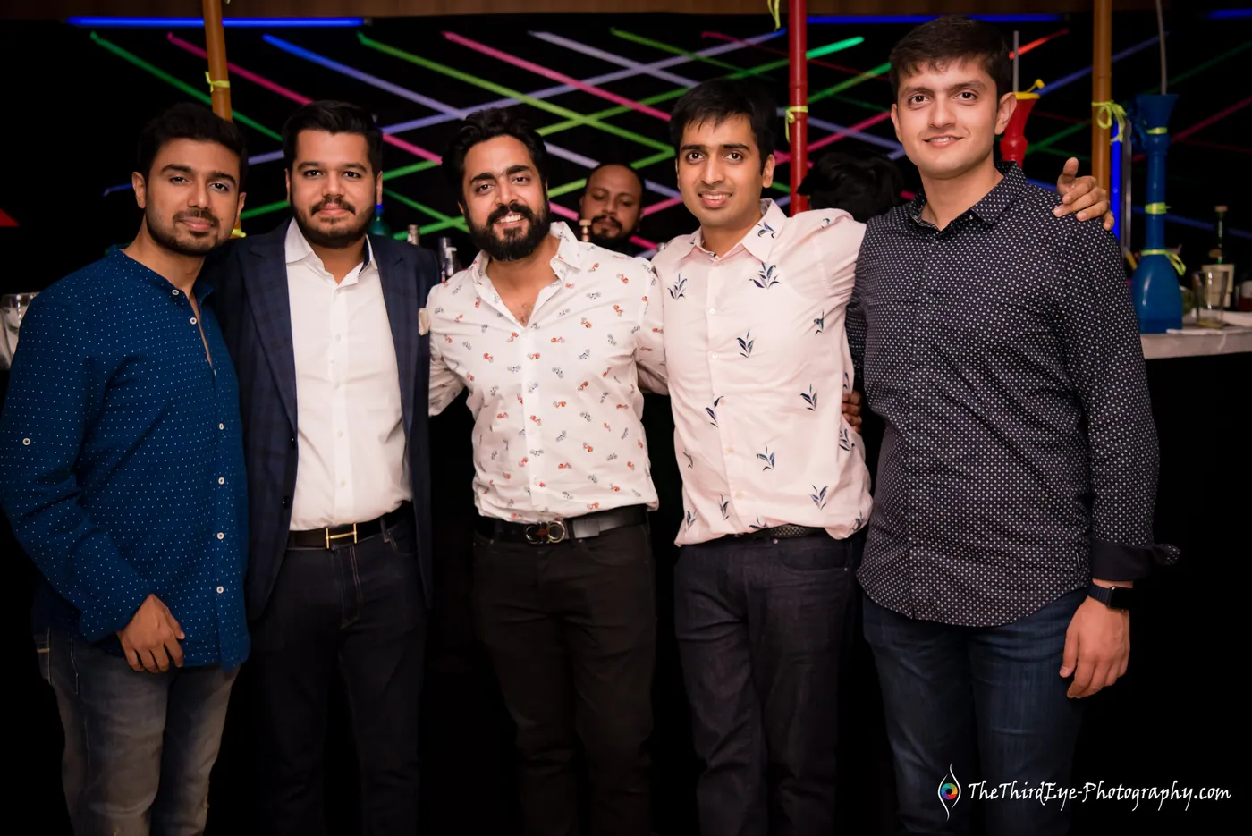 Five men stand shoulder to shoulder with arms around each other against glowing laser lines