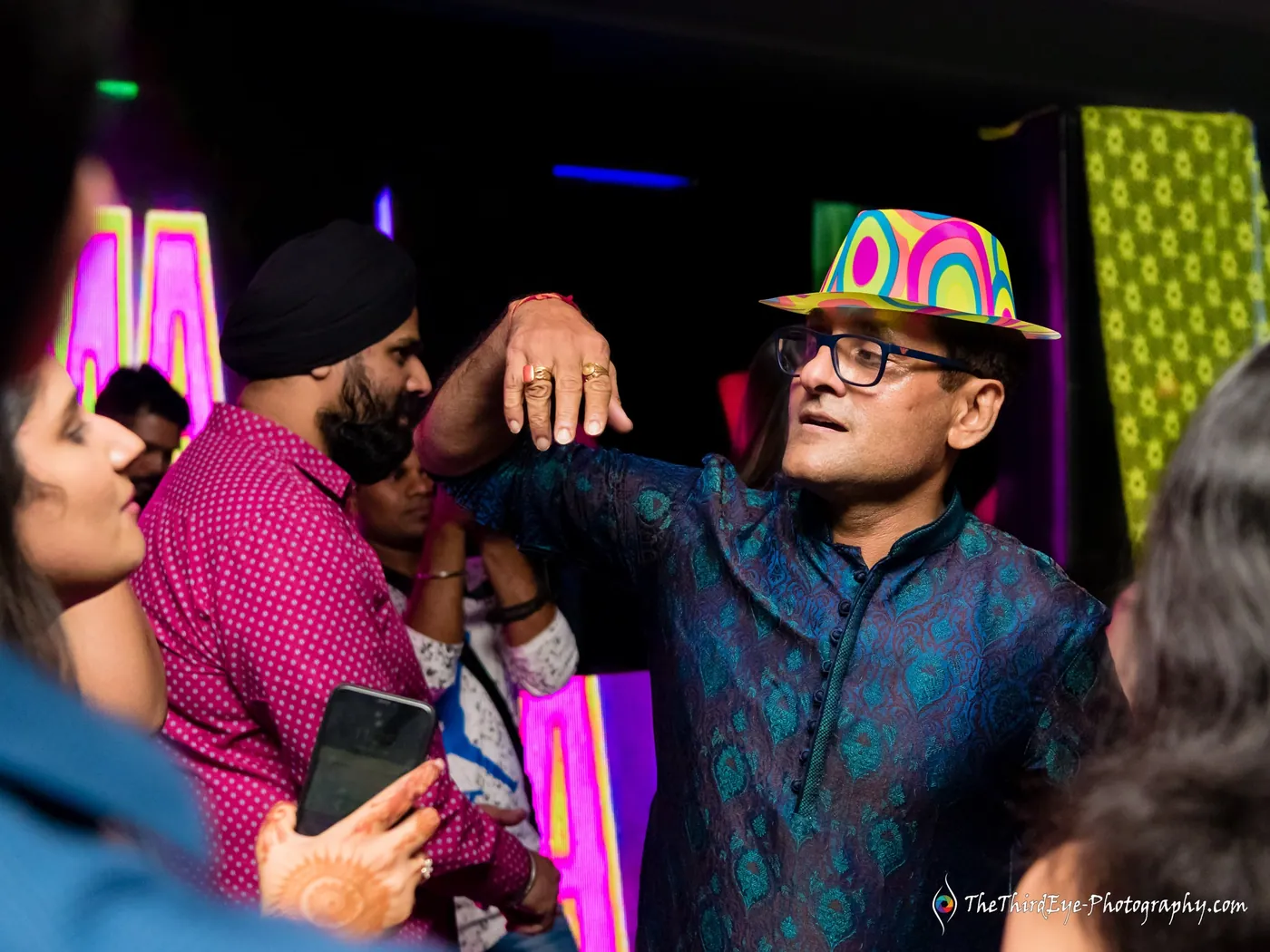 A crowd mid dance with men in hats and a turban, one grinning with a hand on another's shoulder