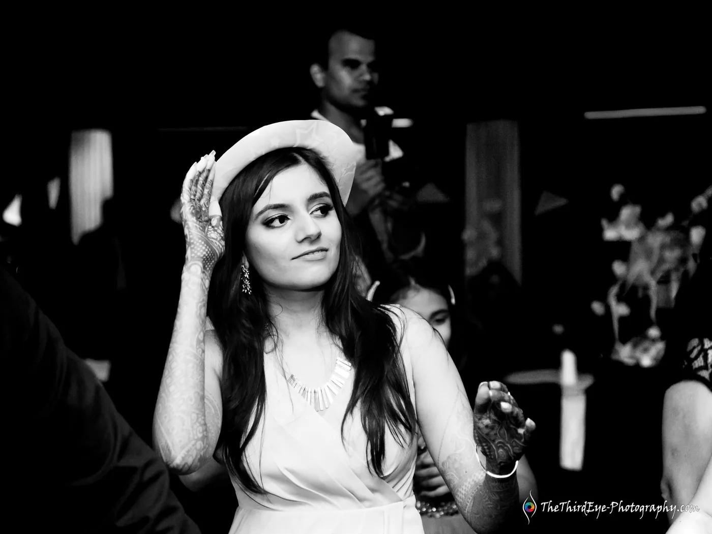 Black and white frame of a woman in a brimmed hat lifting one hand to her ear, looking off camera