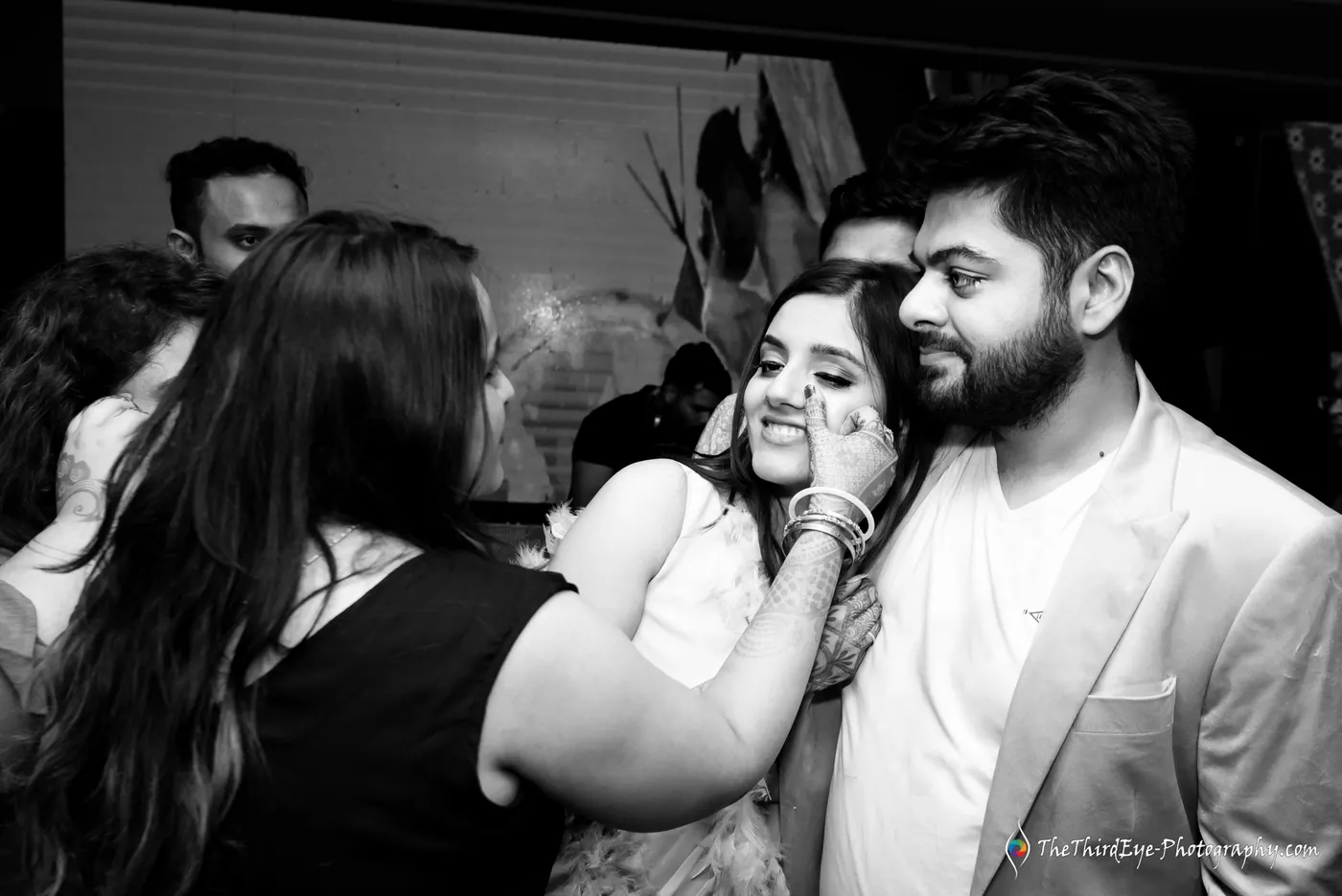 Black and white frame of a woman pressing close to a man's cheek while another woman leans in