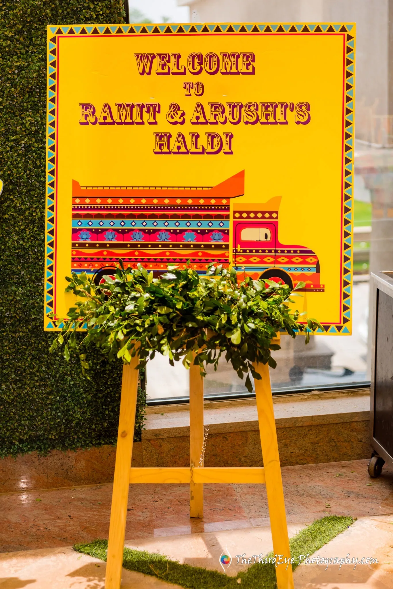 Painted truck style welcome board for Ramit and Arushi's haldi, set on a stand with green leaves at its foot