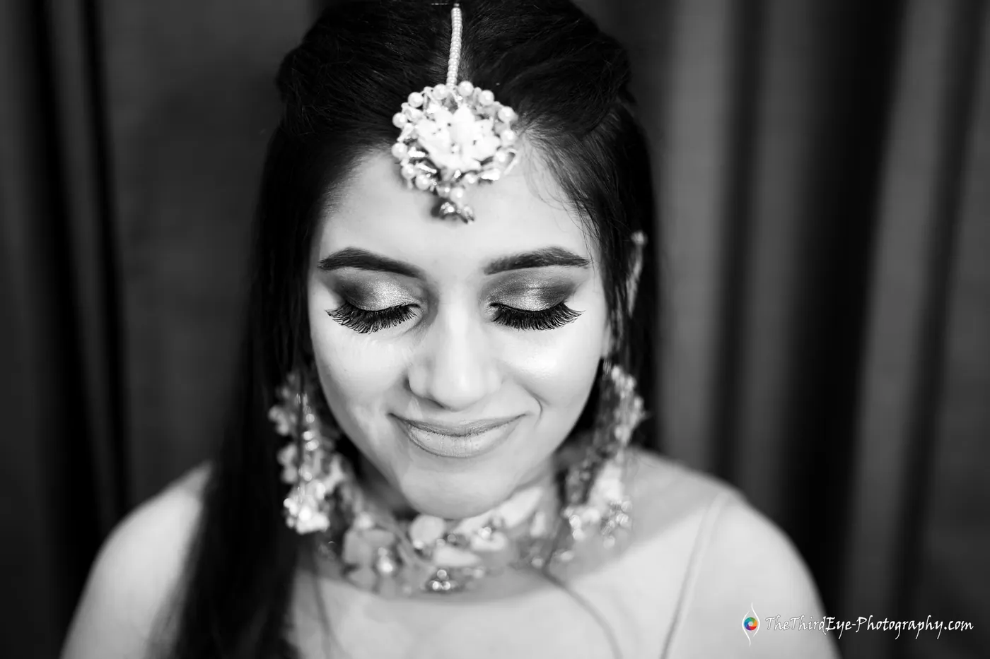 Black and white close portrait of the bride with a maang tikka and shy downcast eyes