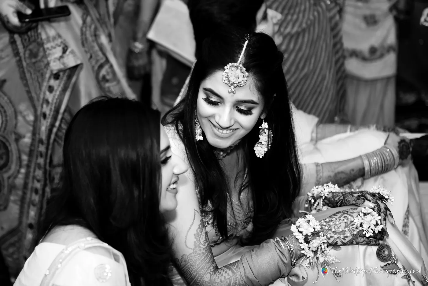 Black and white frame of the bride laughing as a woman leans in close and a third looks on