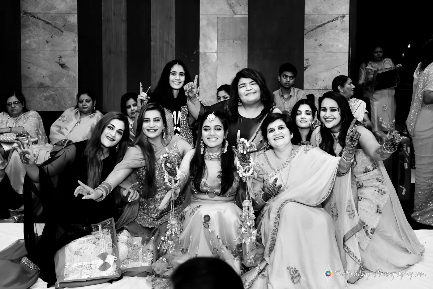 Black and white group of women seated close together on the floor, smiling toward the camera