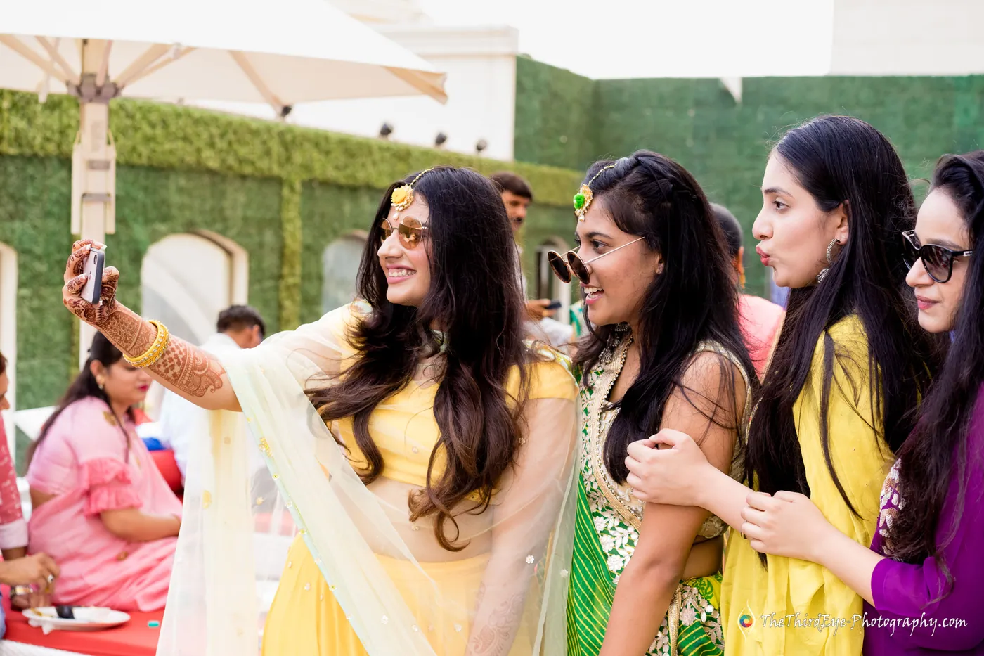 A woman takes a selfie with friends in yellow outfits on the sunlit terrace