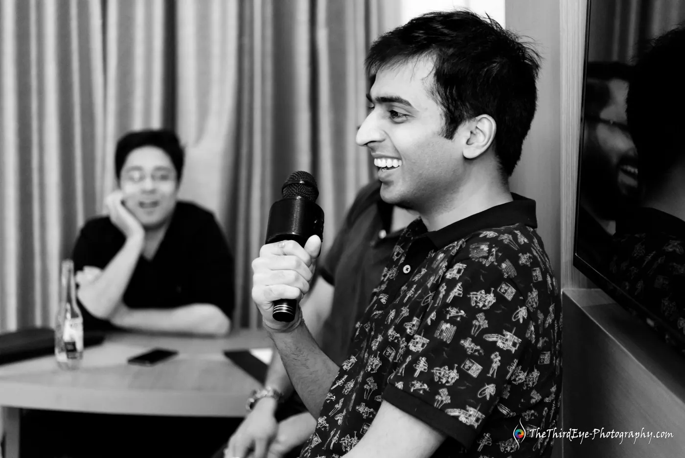 Black and white frame of a man laughing into a microphone while a friend rests his chin on his hand
