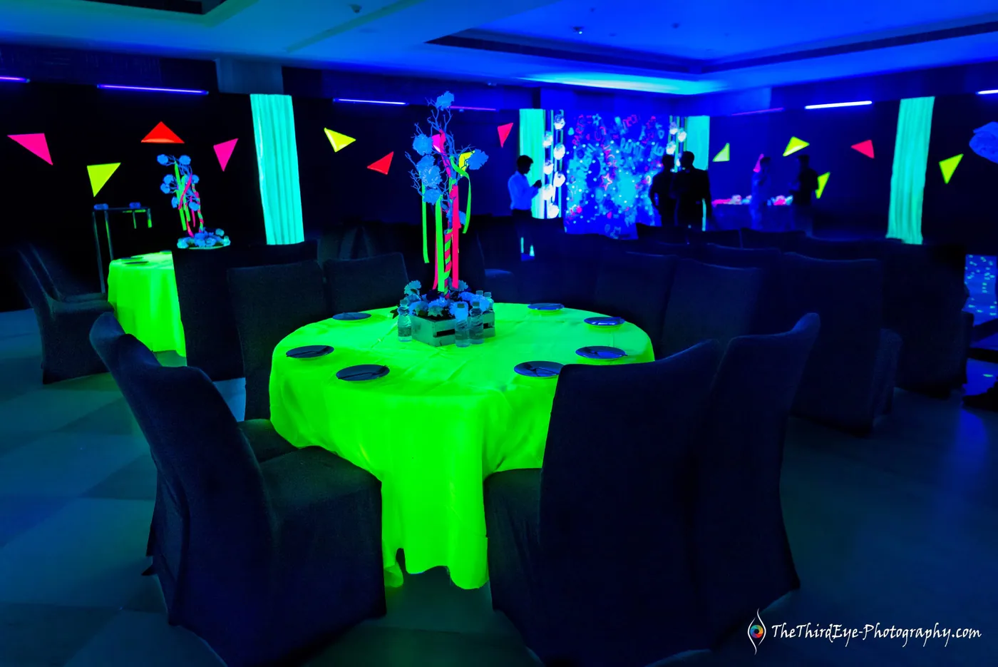 A round table draped in neon green cloth under black light, party flags strung across the dark hall