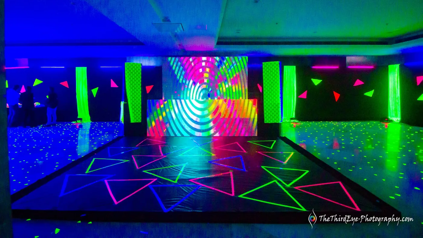Black light dance floor painted with neon stars, green flags and a glowing wall behind it