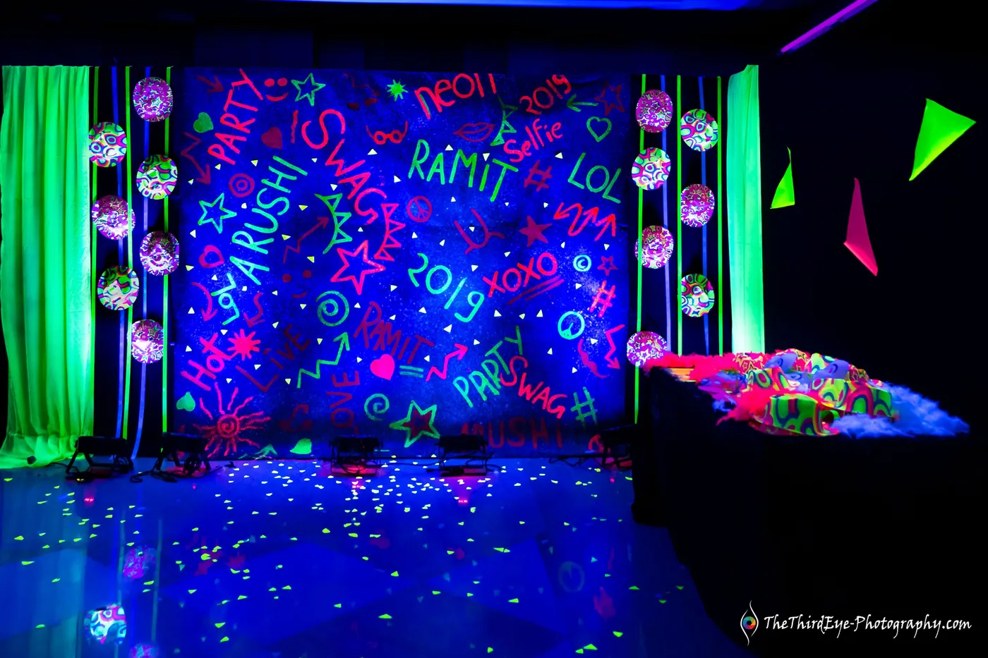 A black light backdrop painted with names and doodles in green and violet, balloons at its base