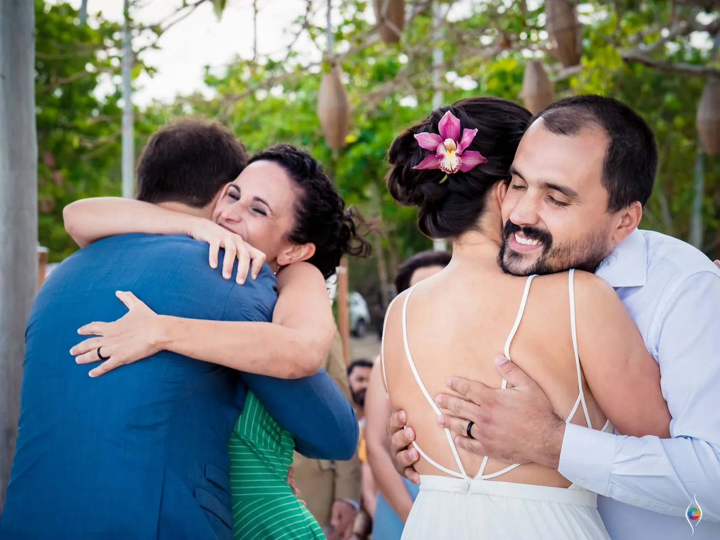Evy hugs a bearded man in a white shirt while a woman in green hugs Thiago beside them