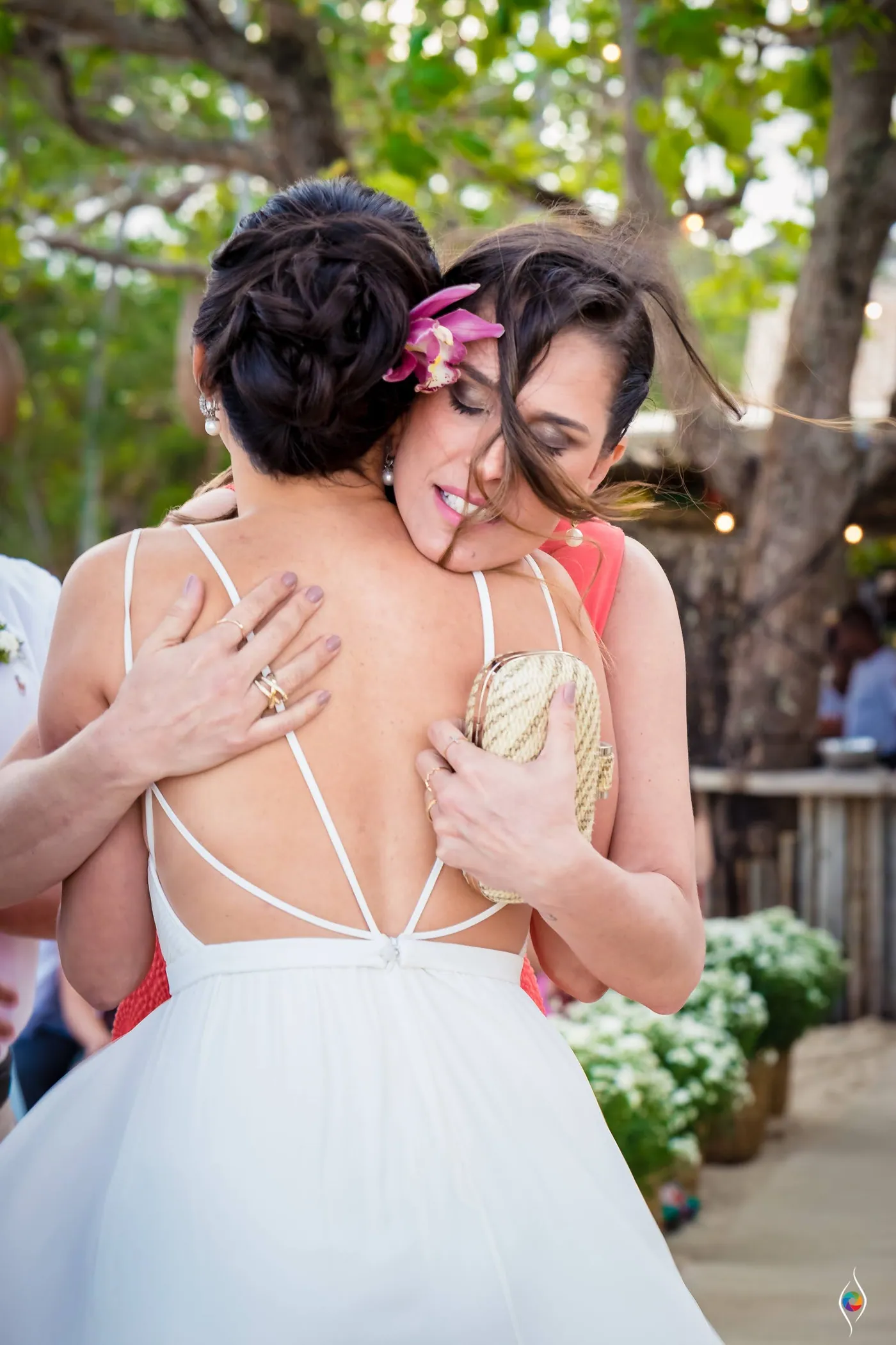 Evy buries her face in the shoulder of a woman in a red dress, an orchid in her hair