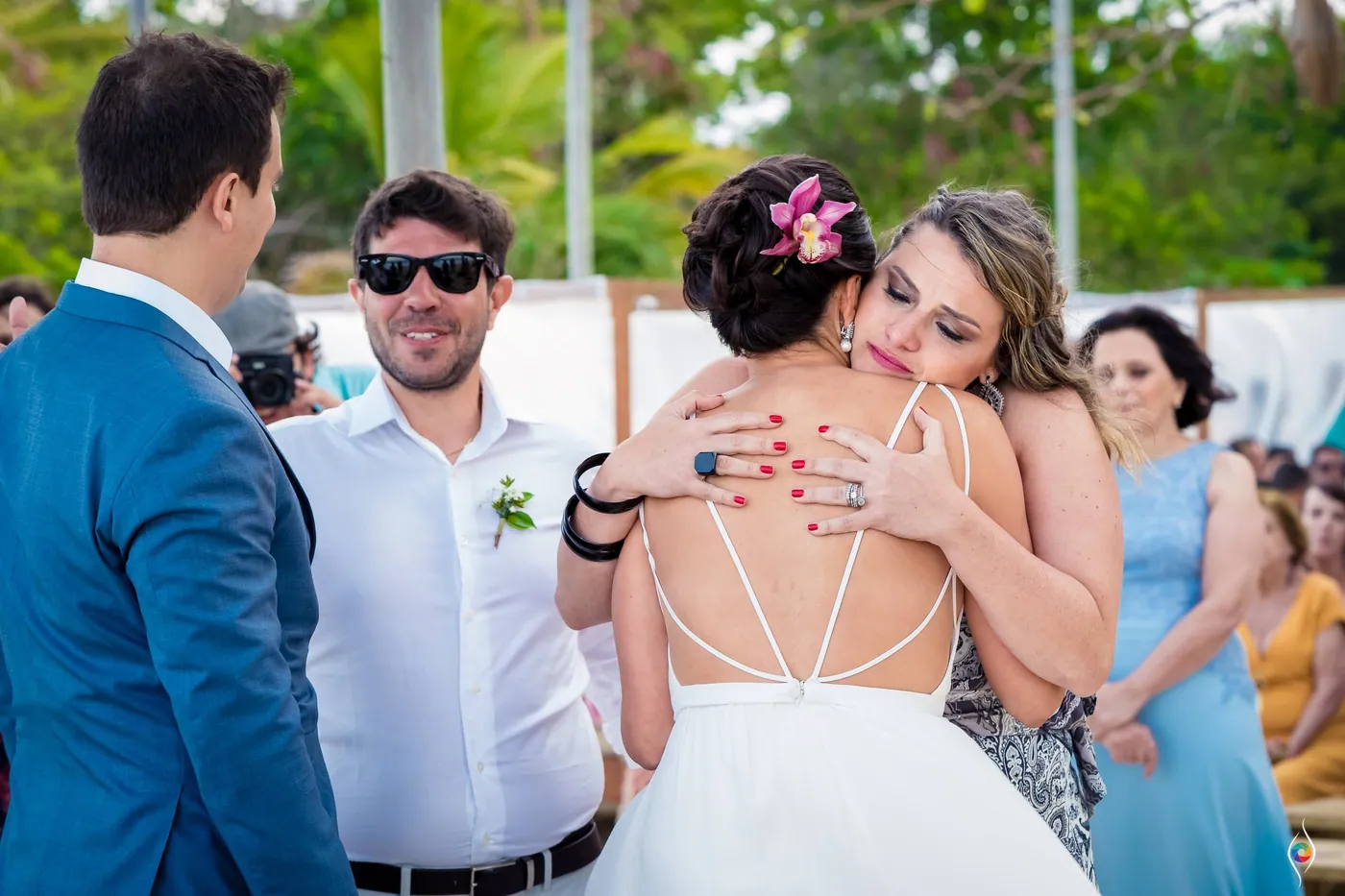 Evy hugs a woman in a flowing dress while Thiago and a man in sunglasses stand beside them