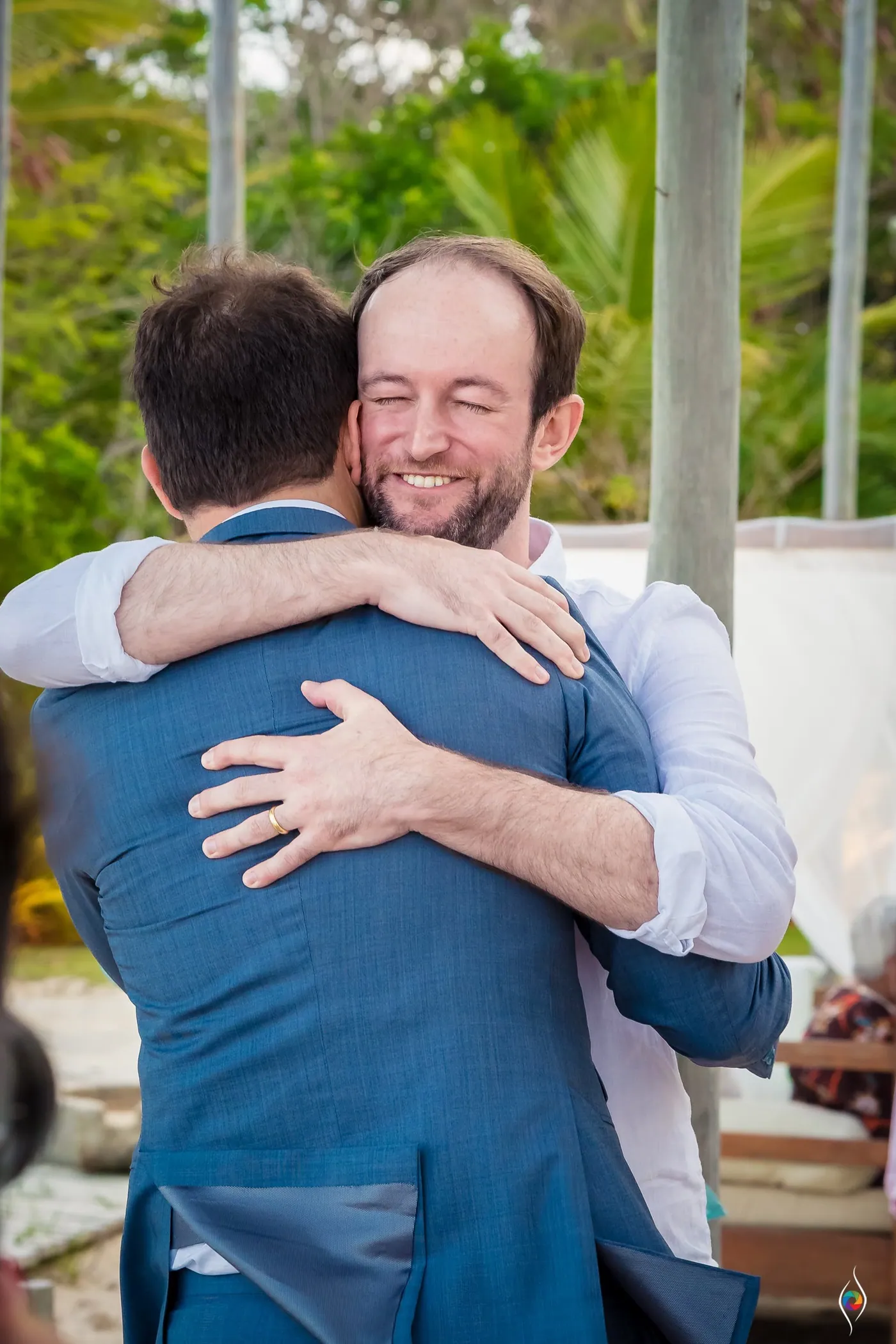 Thiago laughs with his eyes shut in a bear hug with a bearded man in a white shirt