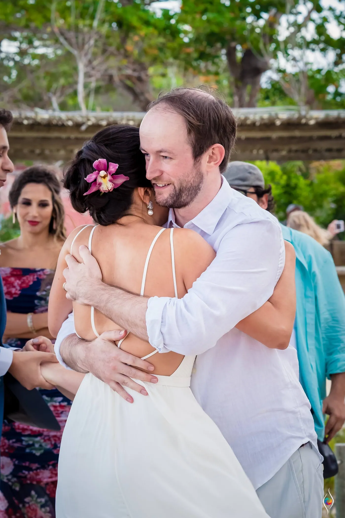 Evy leans into a hug with a bearded man in a white shirt, her orchid bright in her hair