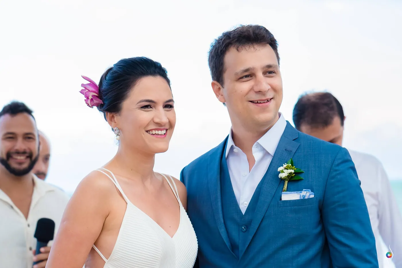 Evy with a pink flower in her hair and Thiago smile broadly as friends stand close behind