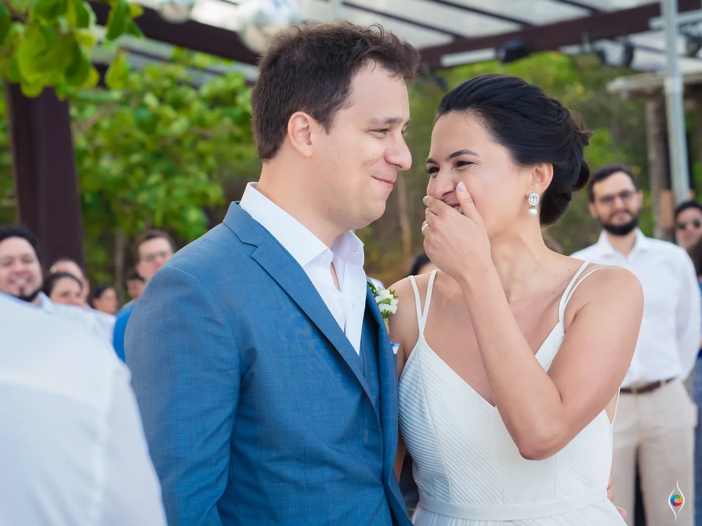 Evy covers her mouth as she laughs while Thiago grins and looks down, guests packed behind them