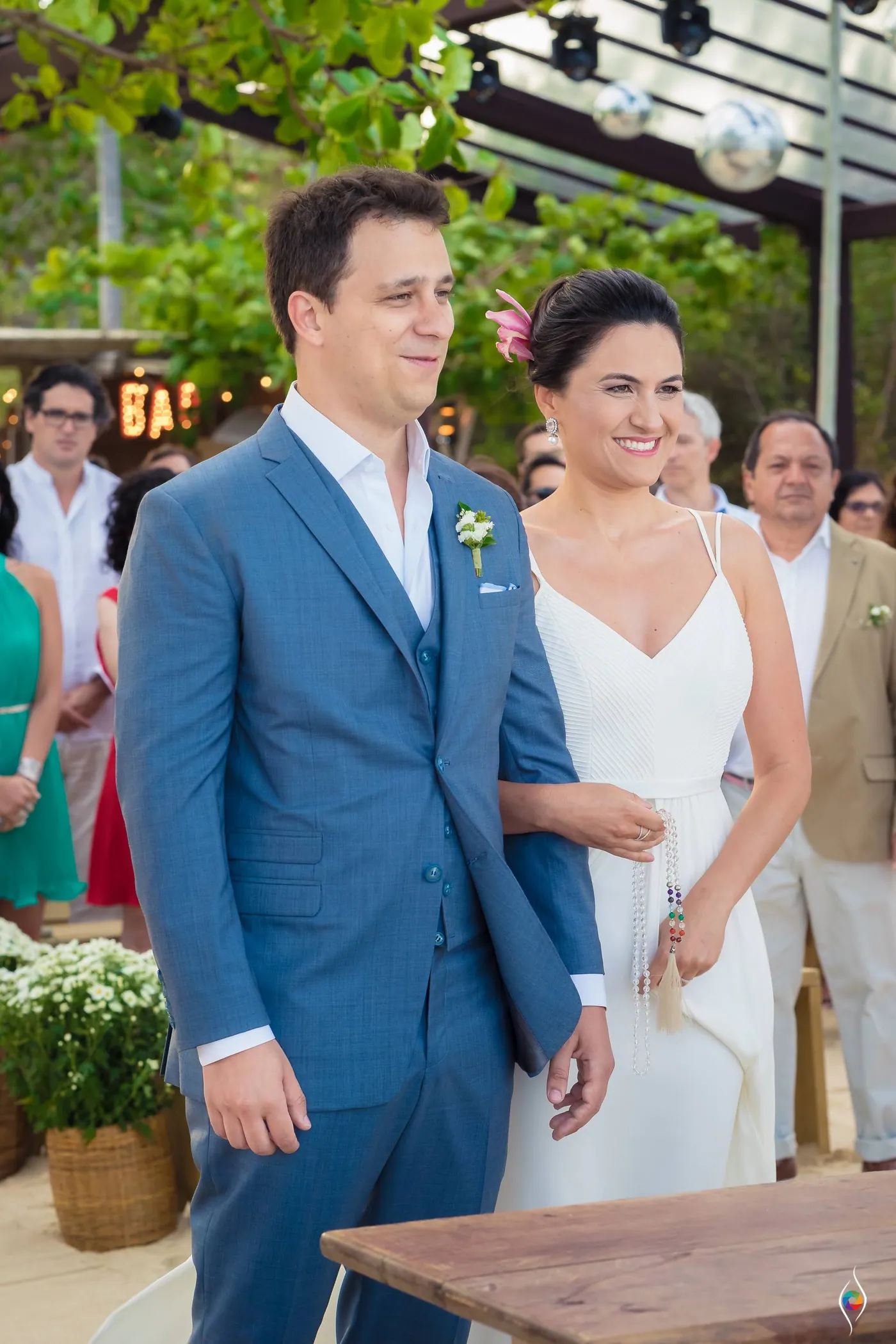 Thiago looks ahead with a calm smile as Evy glances aside, a wooden table at the edge of frame