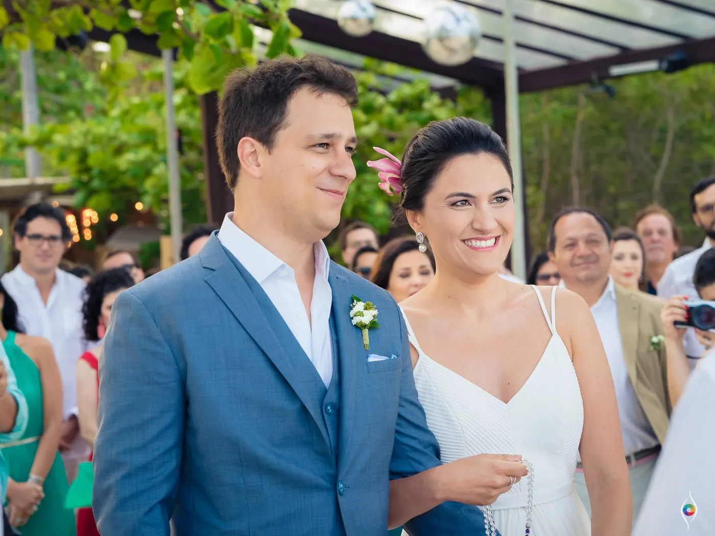 Evy and Thiago smile gently side by side while rows of guests watch from behind