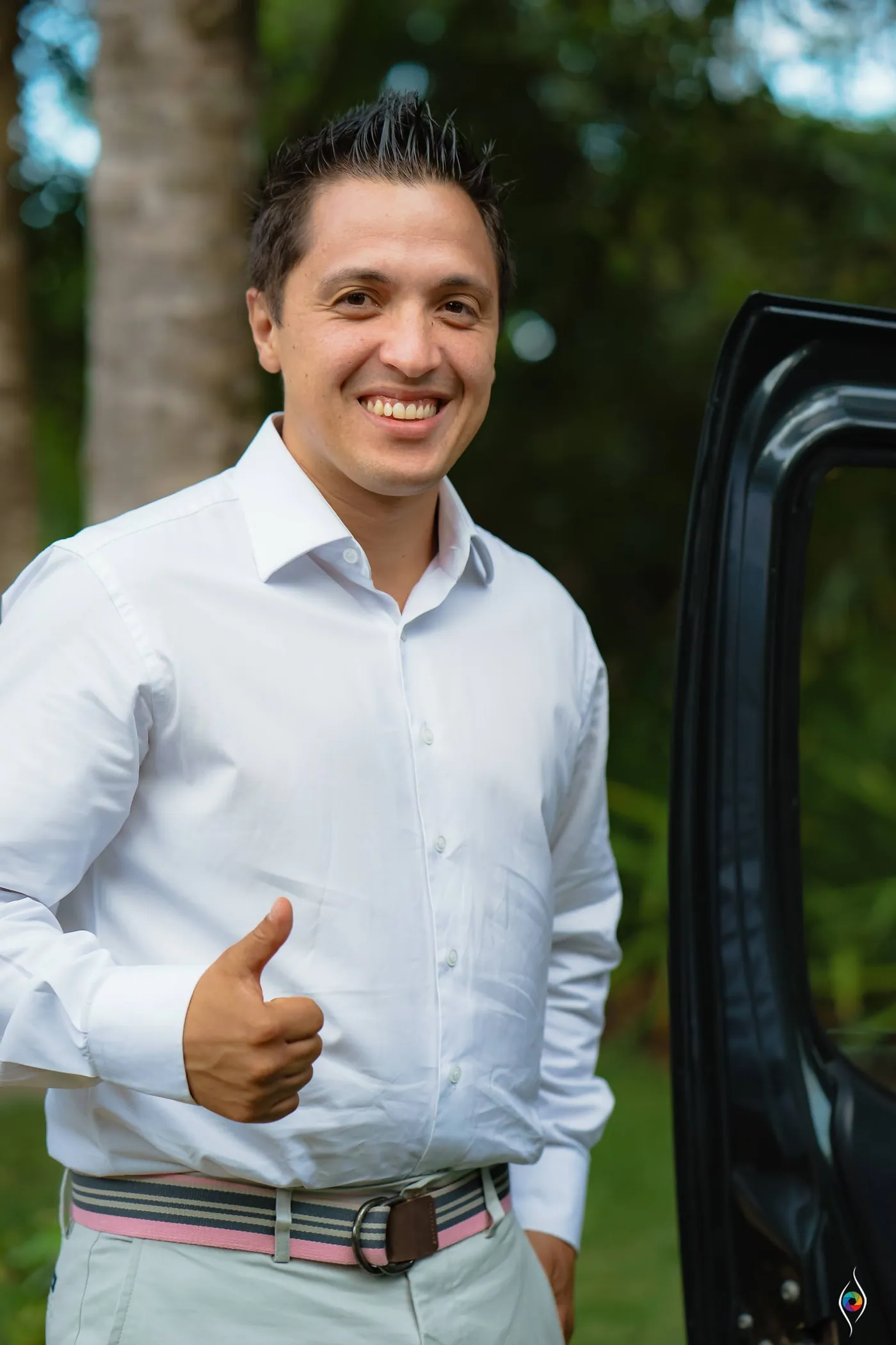 A man in a white shirt gives a thumbs up beside an open van door with trees behind him