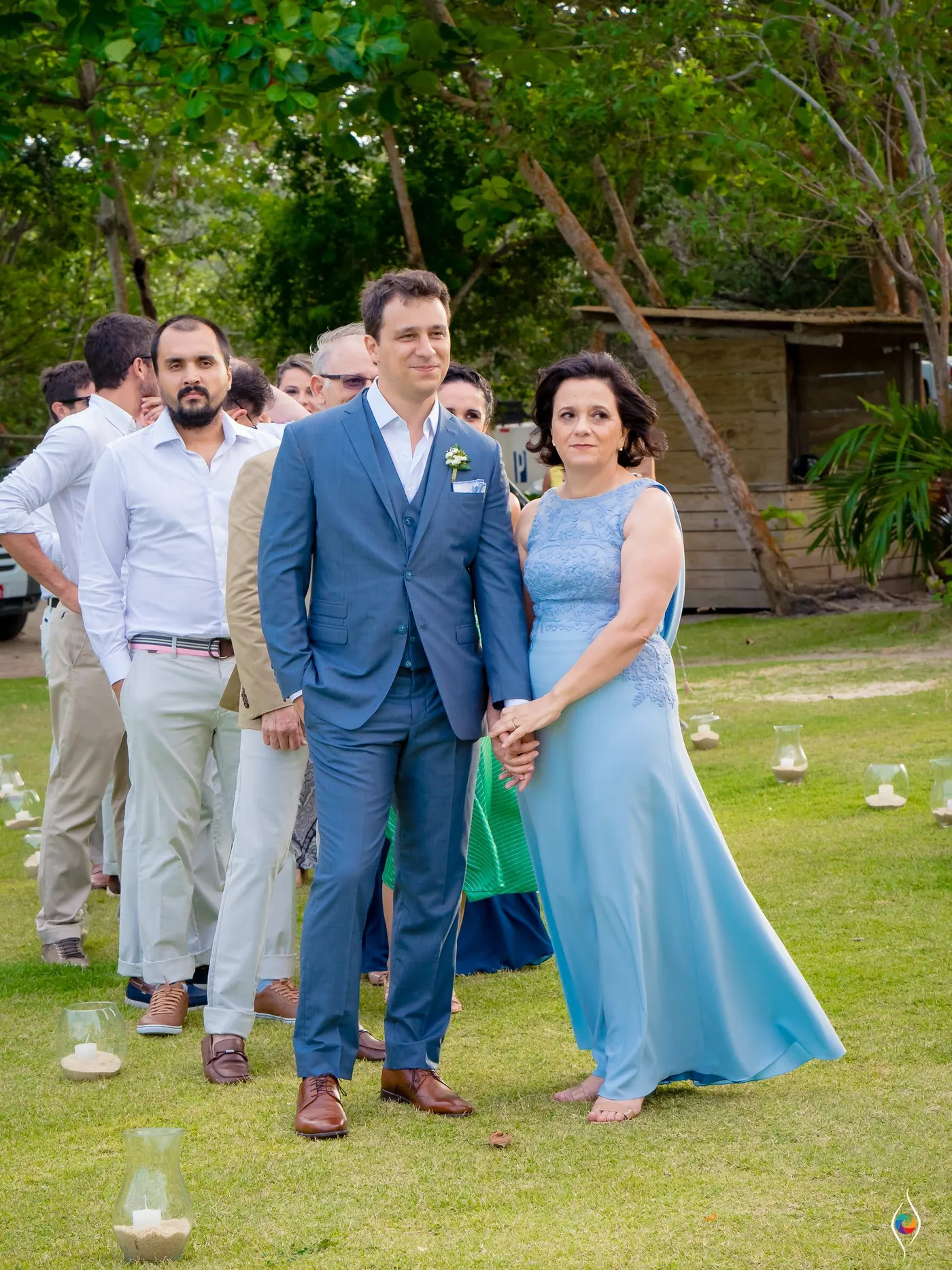 Thiago in a blue suit waits on the lawn as a woman in pale blue stands beside him