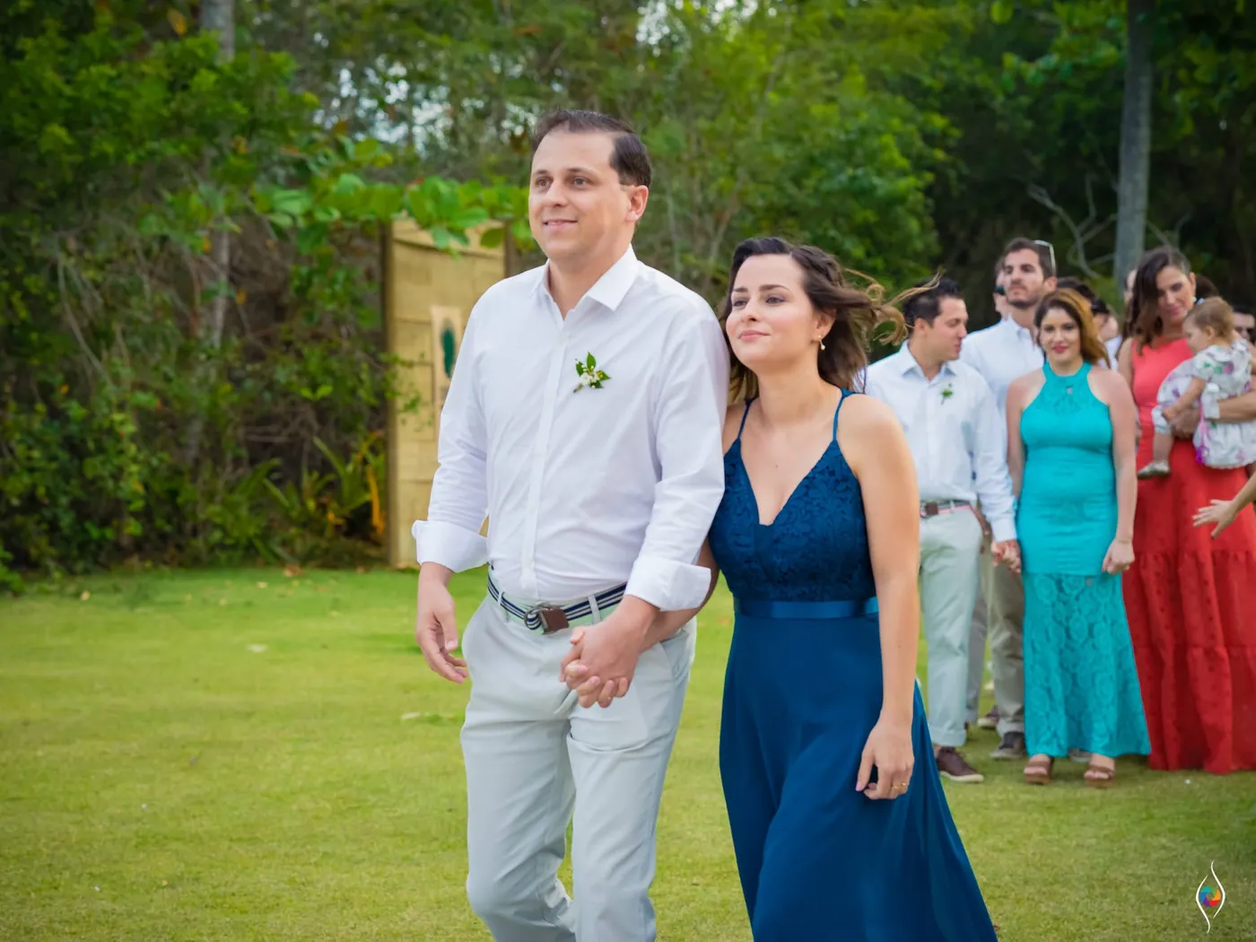 A man in a white shirt and a woman in a navy dress walk hand in hand across the lawn