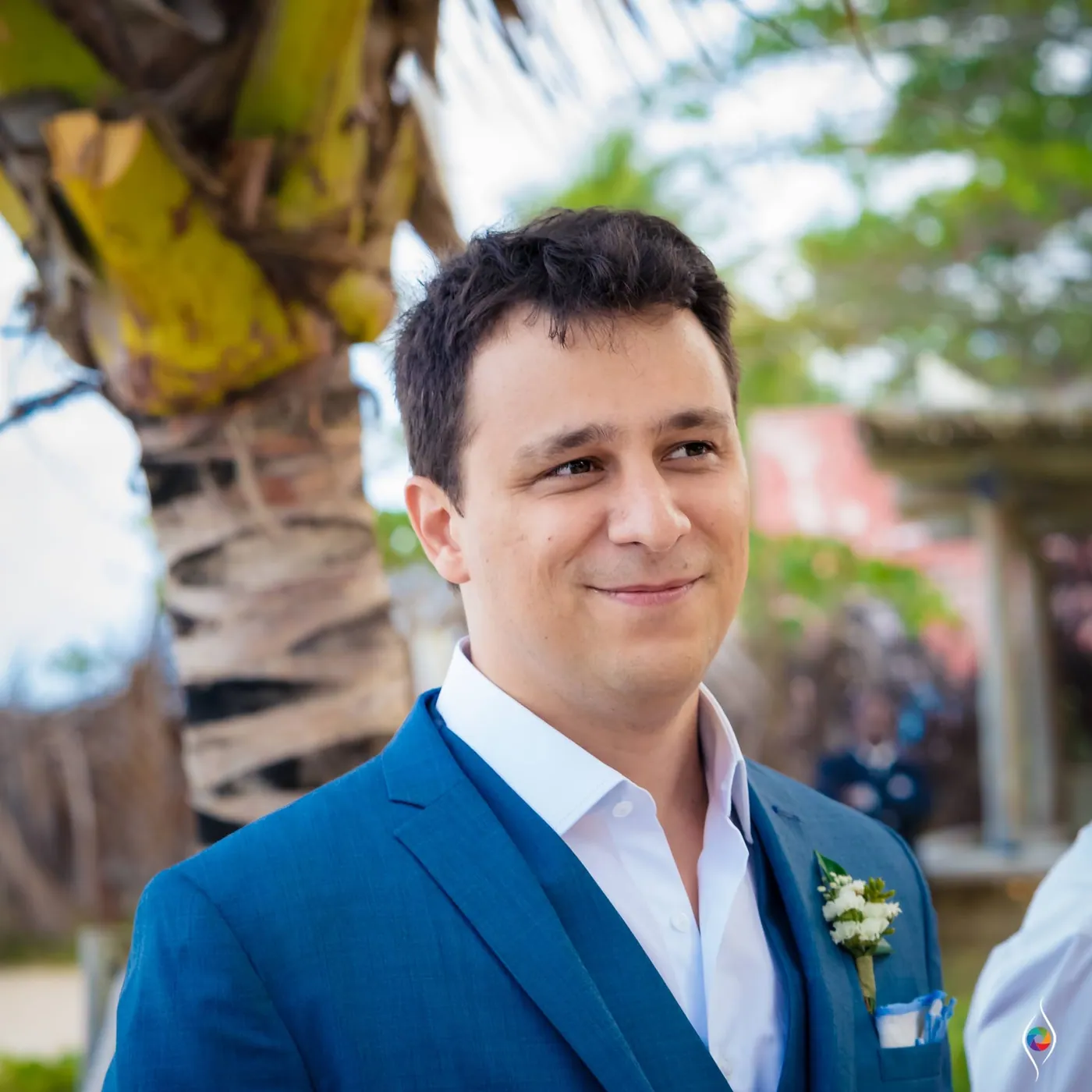 Close portrait of Thiago smiling softly past the camera, a palm trunk behind him