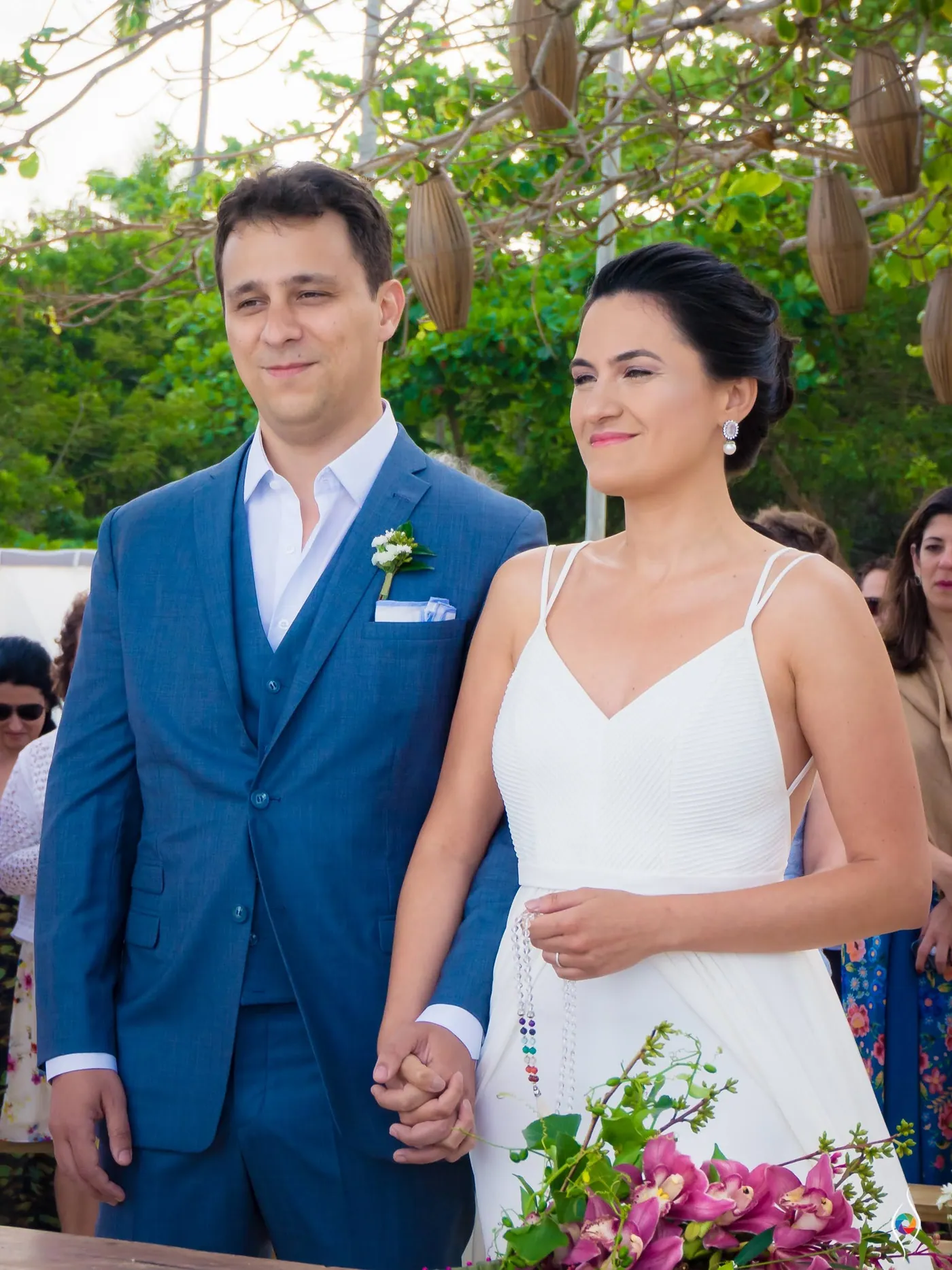 Evy and Thiago stand hand in hand beside the wooden table, both looking ahead
