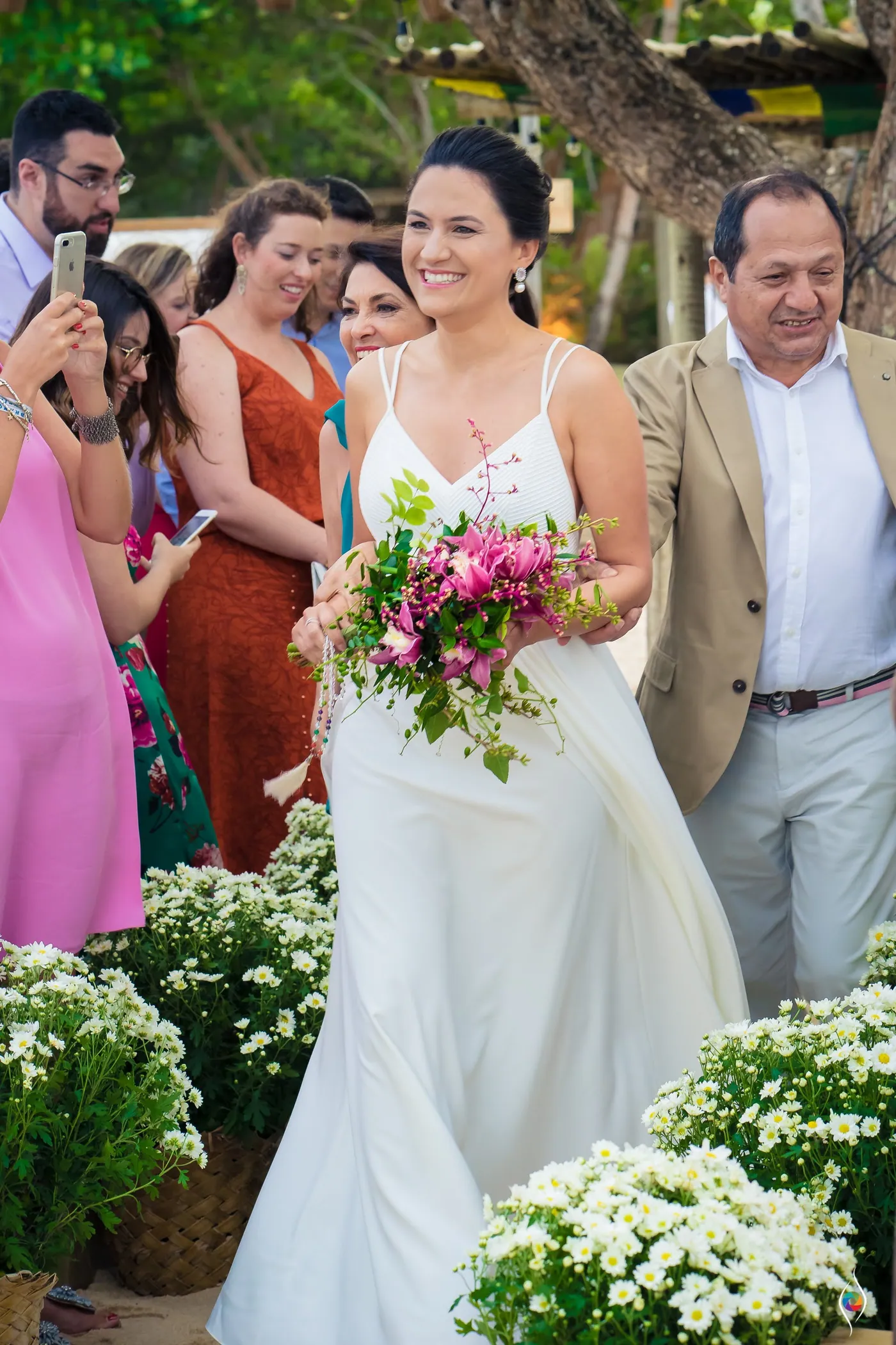 Evy walks down the aisle with a bouquet of pink flowers, a man in a tan jacket beside her