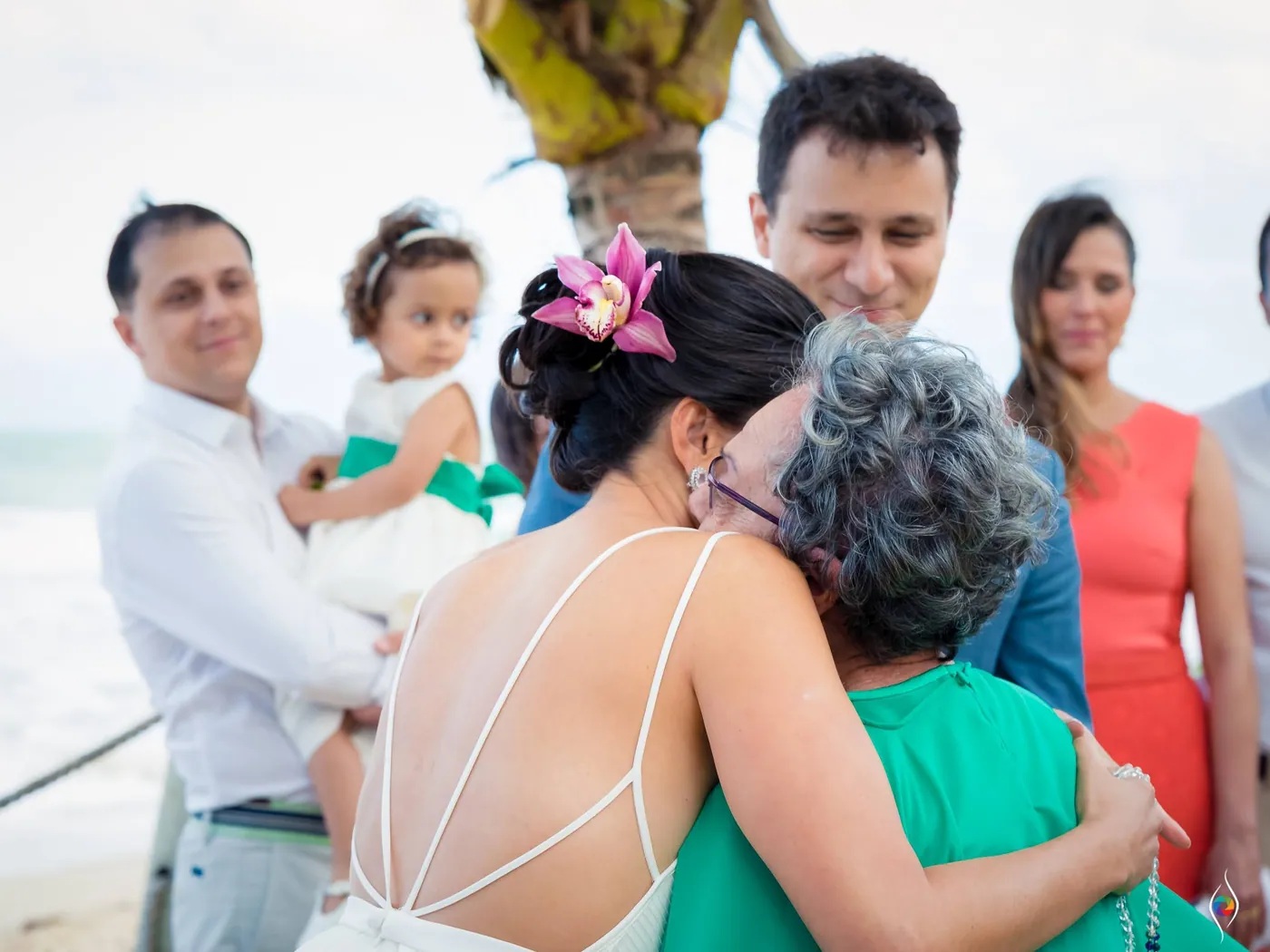 Evy in a close embrace with an older woman in green, a toddler held up in a guest's arms behind them