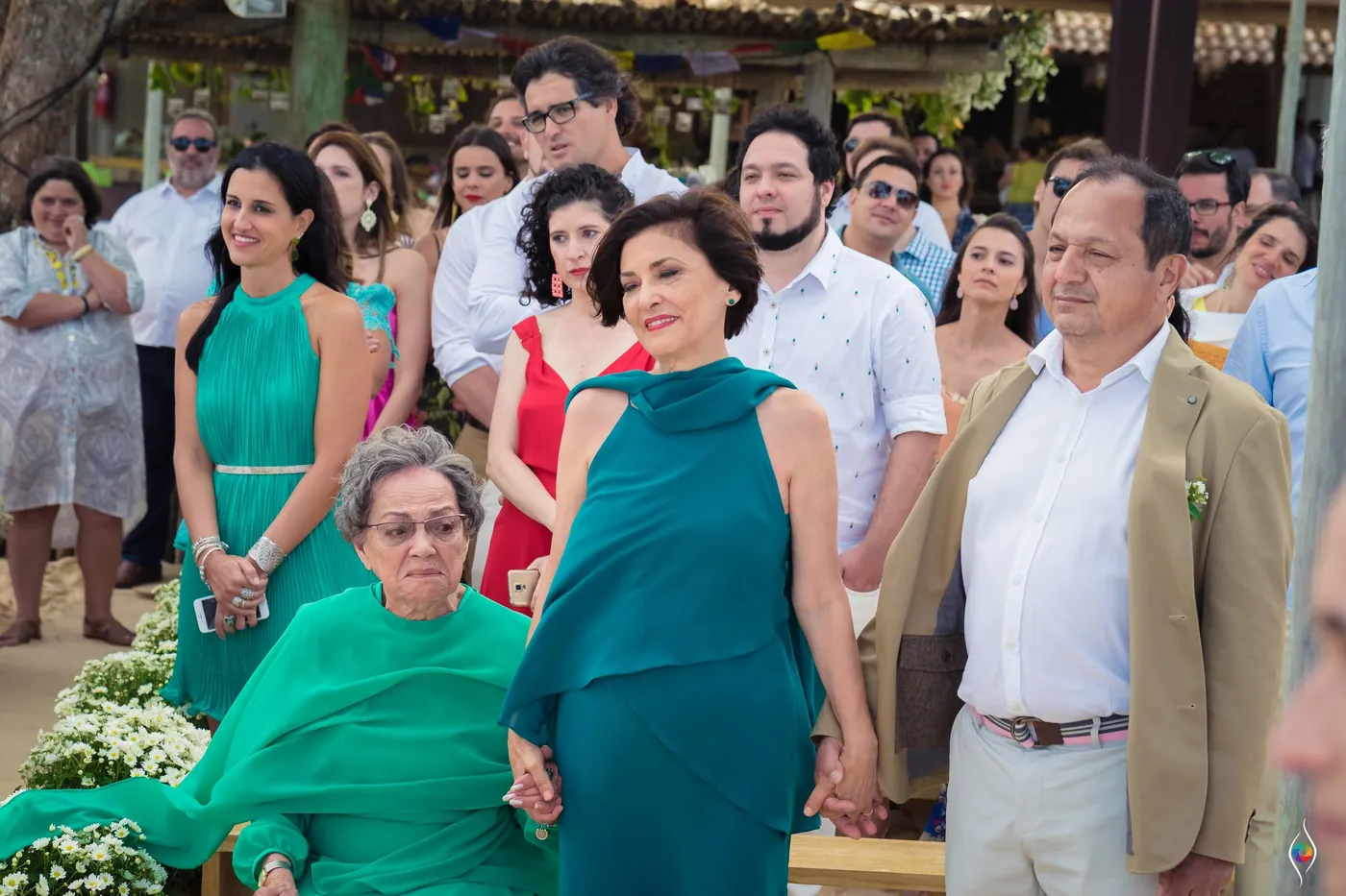 A woman in teal holds hands with a man in a tan jacket while an older woman sits in green nearby