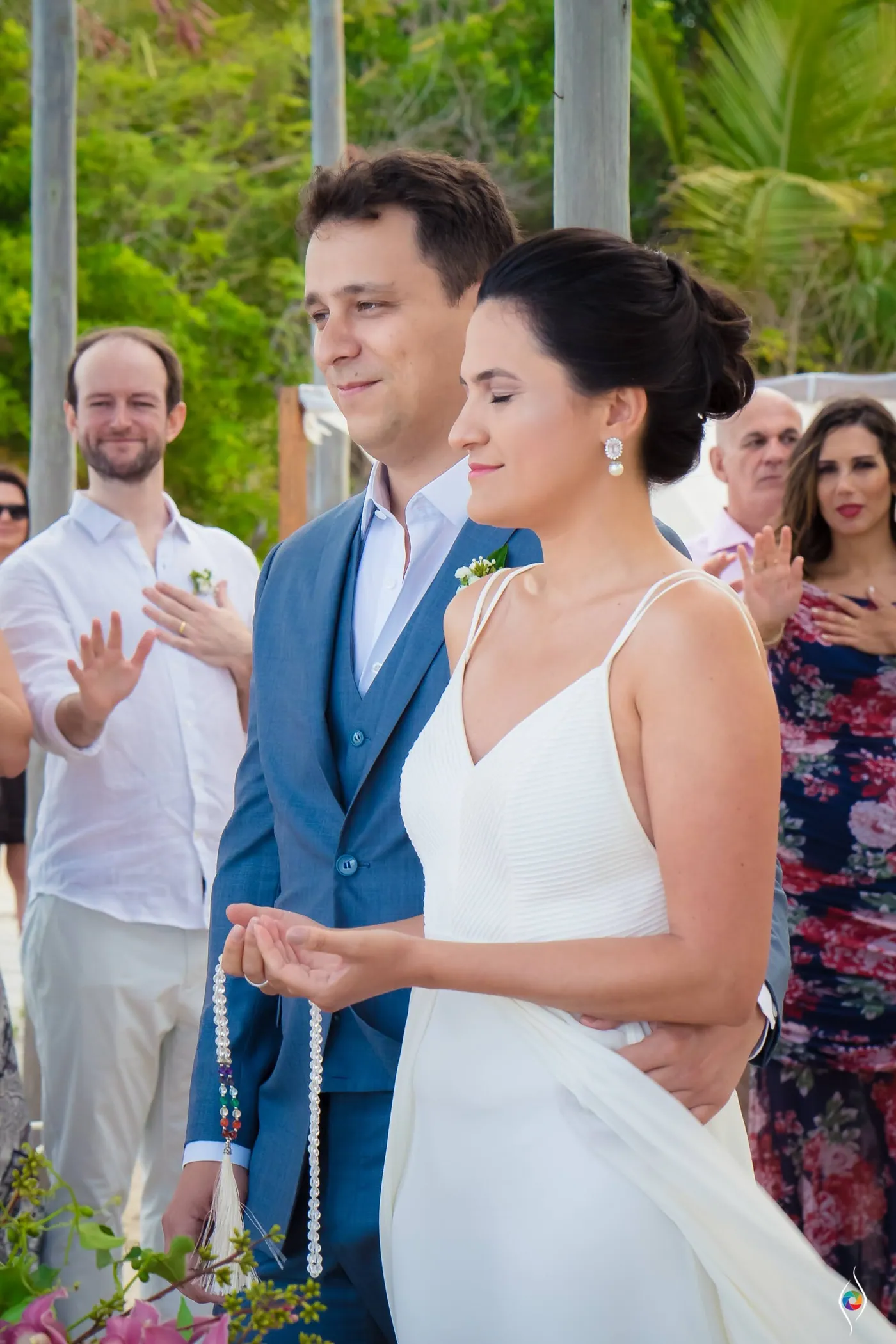 Evy and Thiago stand shoulder to shoulder while he holds a string of beads in his palm