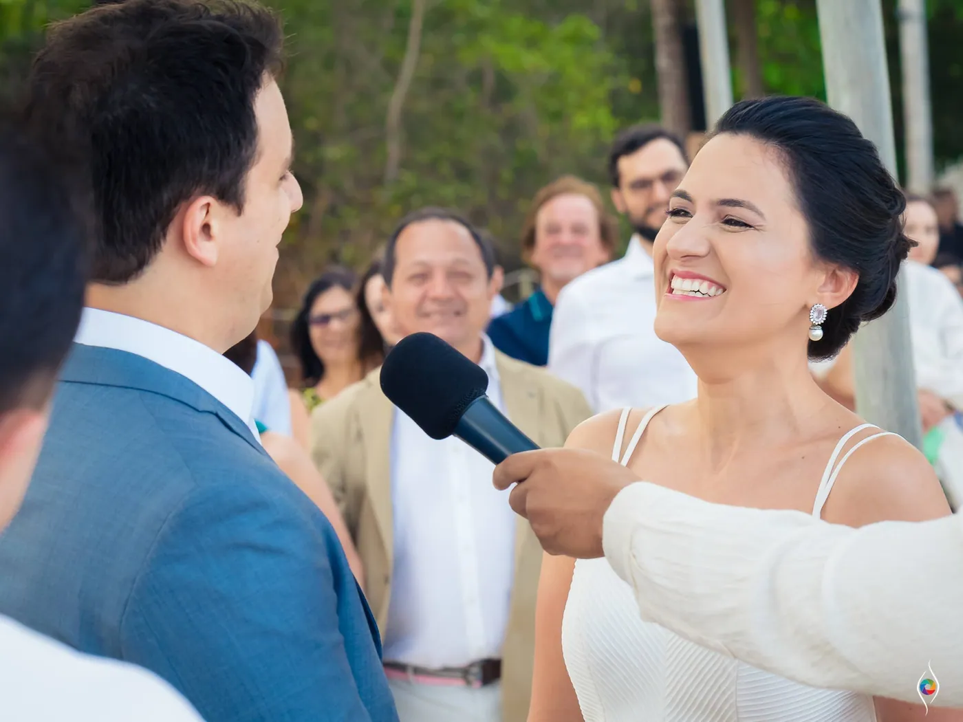 Evy beams as a man in white holds a microphone toward her and Thiago