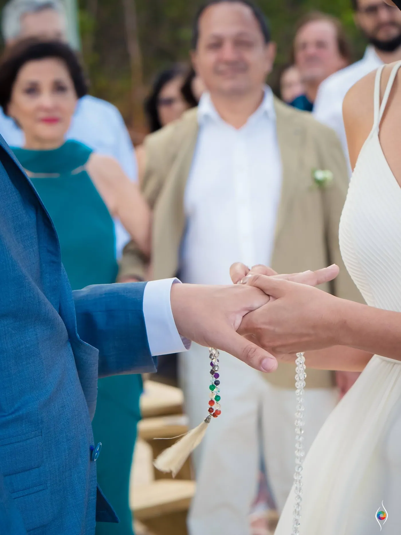 Evy's and Thiago's clasped hands hold colourful beads against her white dress