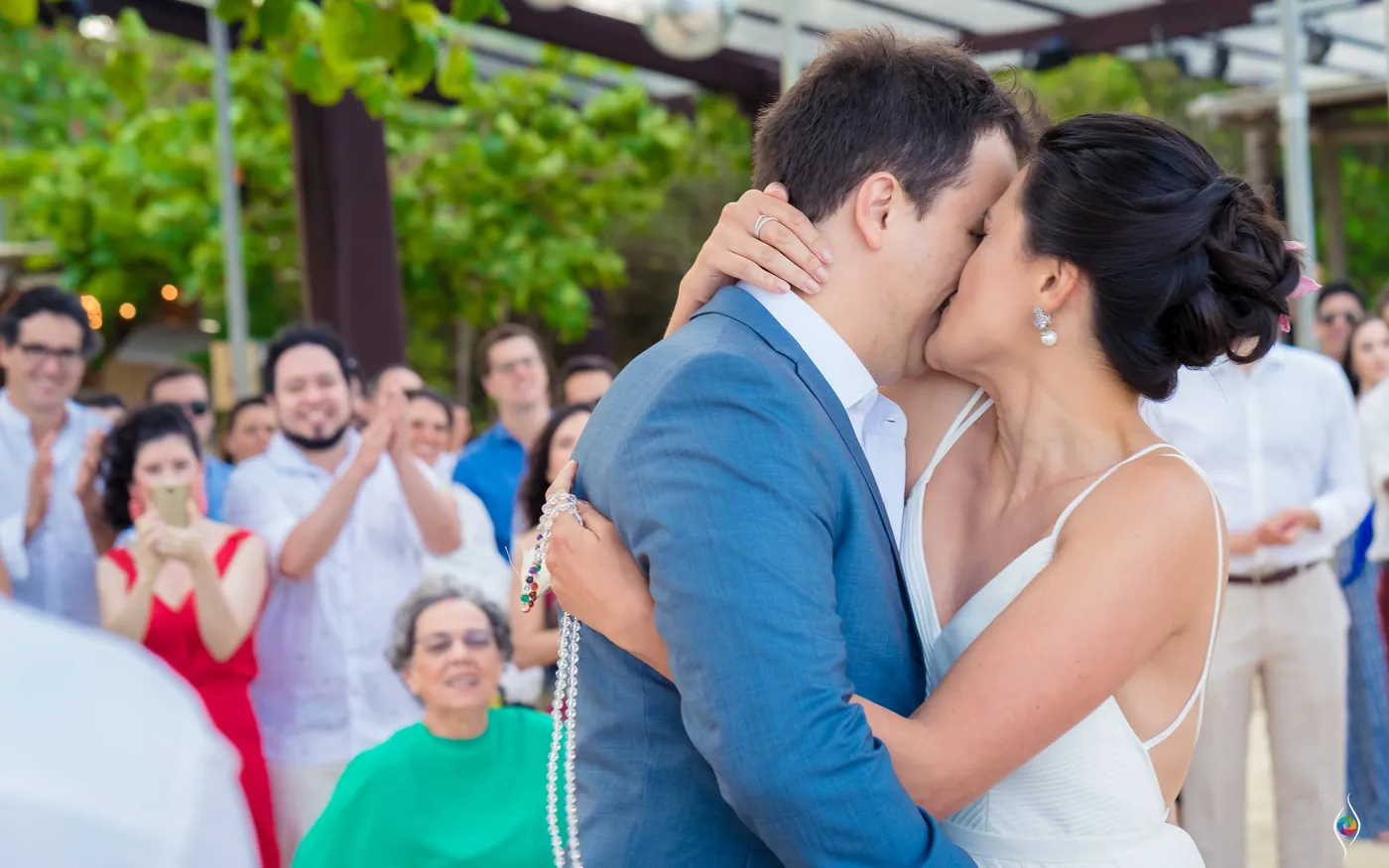 Thiago and Evy kiss as guests applaud, a woman in green watching at the bottom of the frame