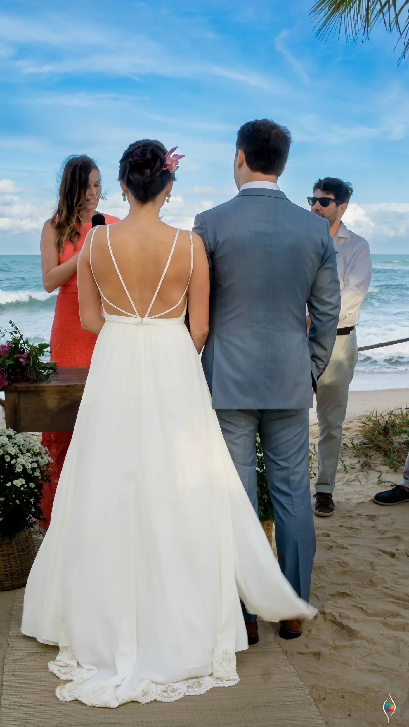 Evy in her long white dress seen from behind beside a man in a grey suit with the sea ahead