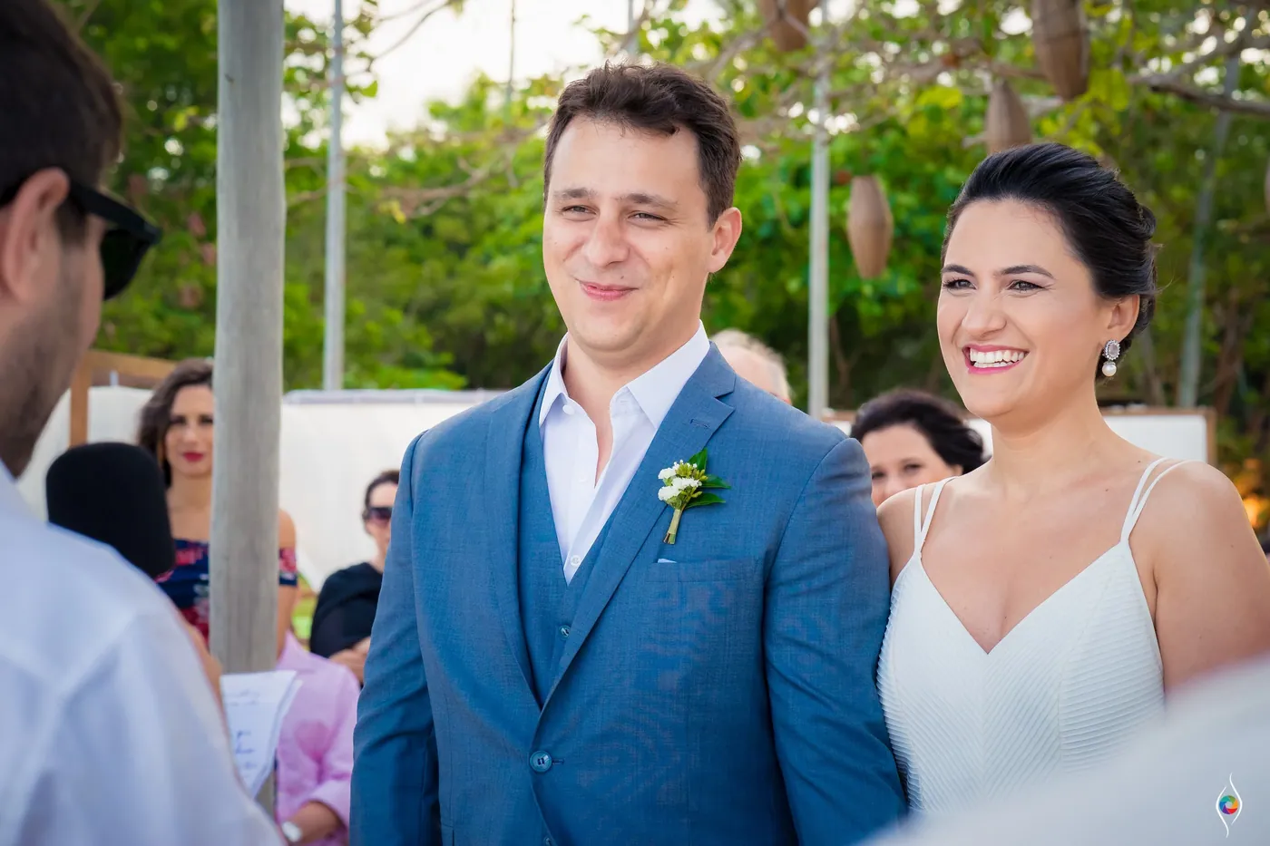 Thiago smiles with crinkled eyes while Evy beams beside him, guests clustered behind