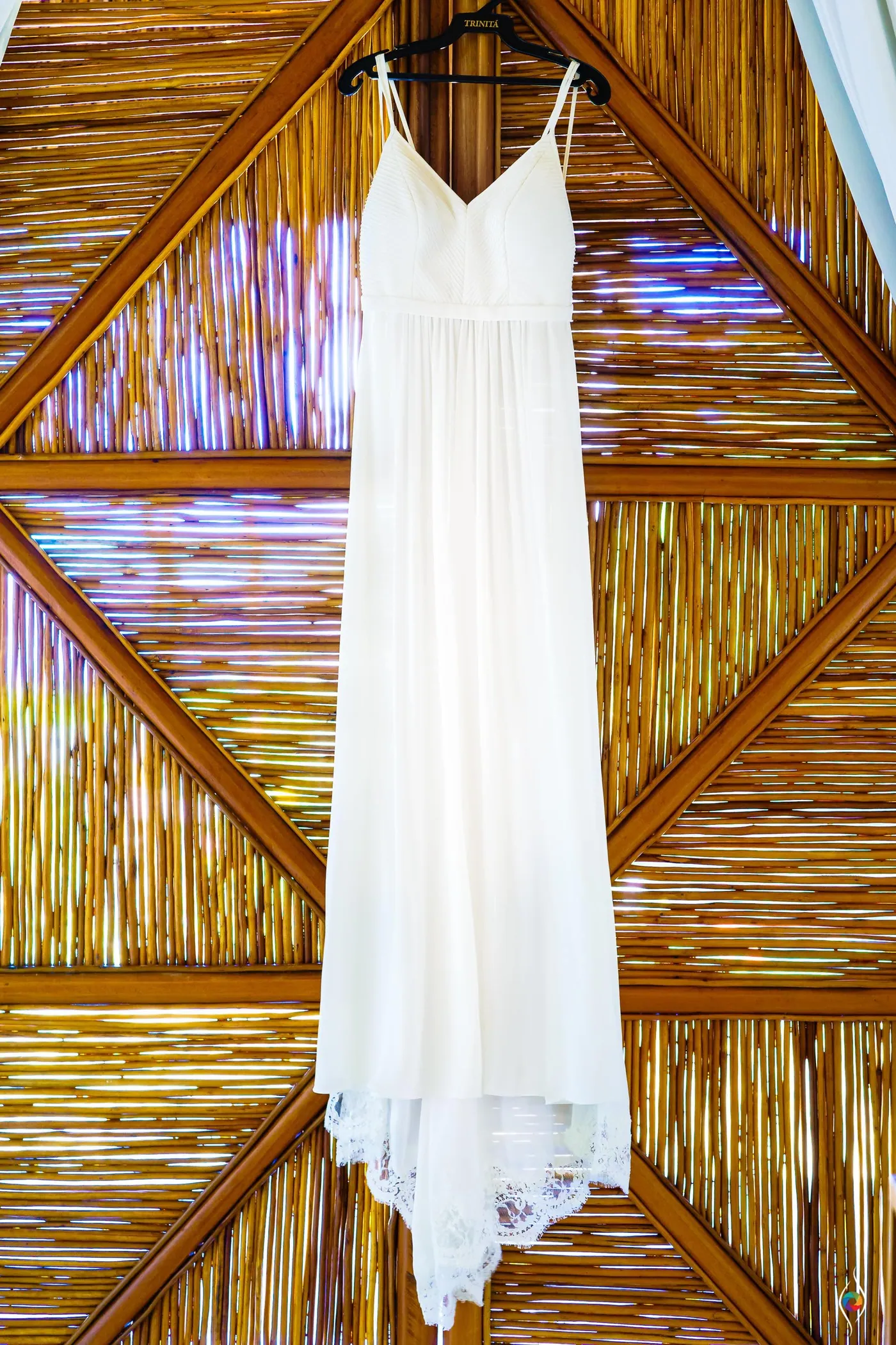 A white wedding dress hangs against a woven bamboo door
