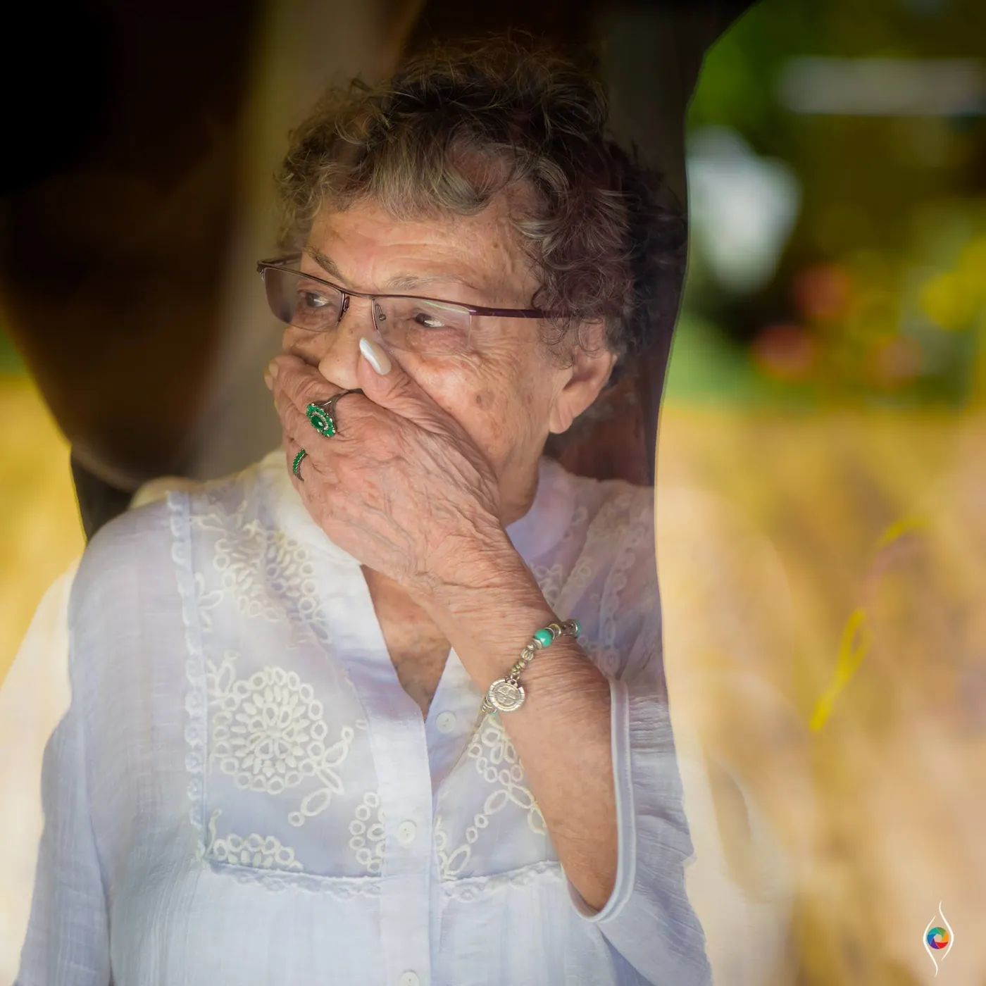 An older woman laughs with a hand over her mouth, golden grass blurred around her