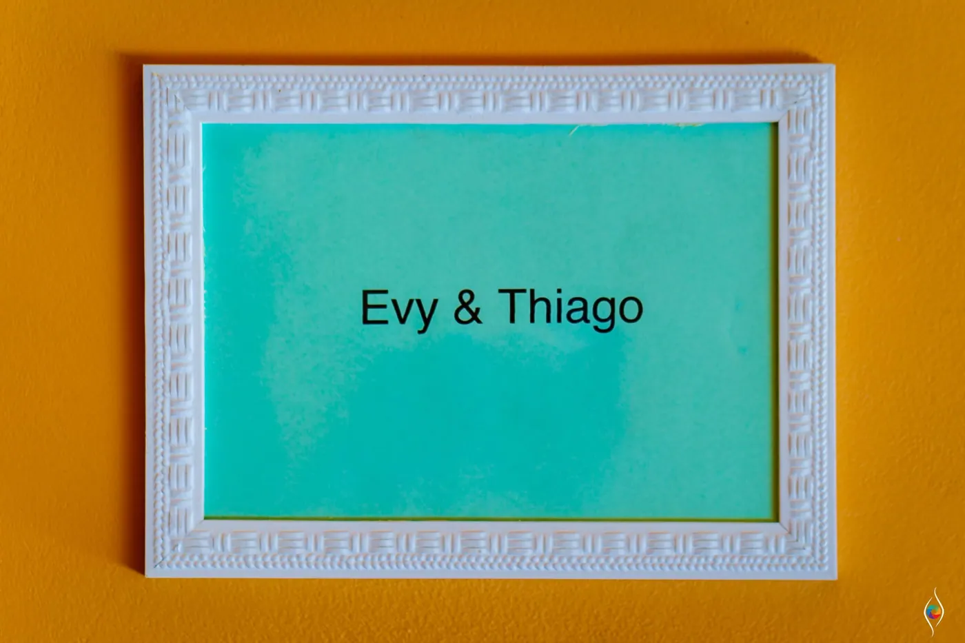 Framed teal sign reading Evy and Thiago on a bright orange wall