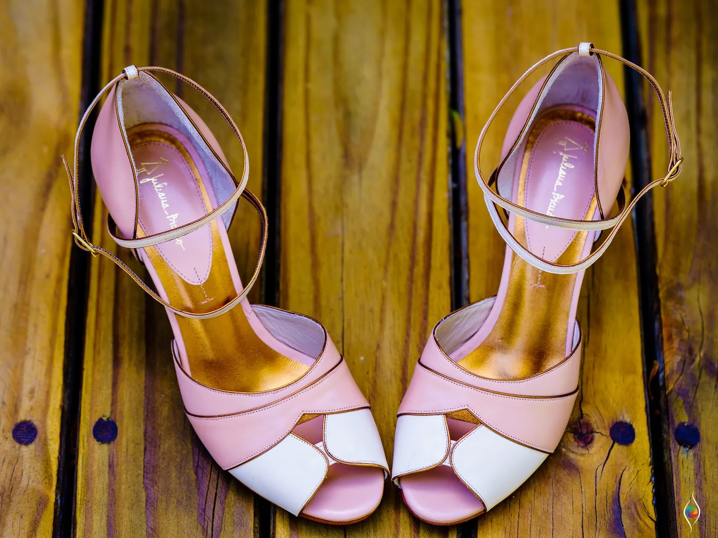 Pink and white strappy heels on a dark wooden floor in warm light
