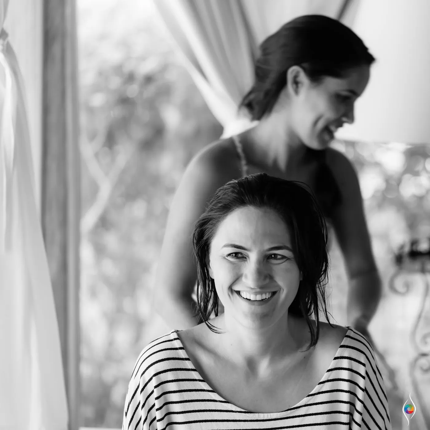 Evy smiles in a striped top while a hairstylist works behind her, in black and white