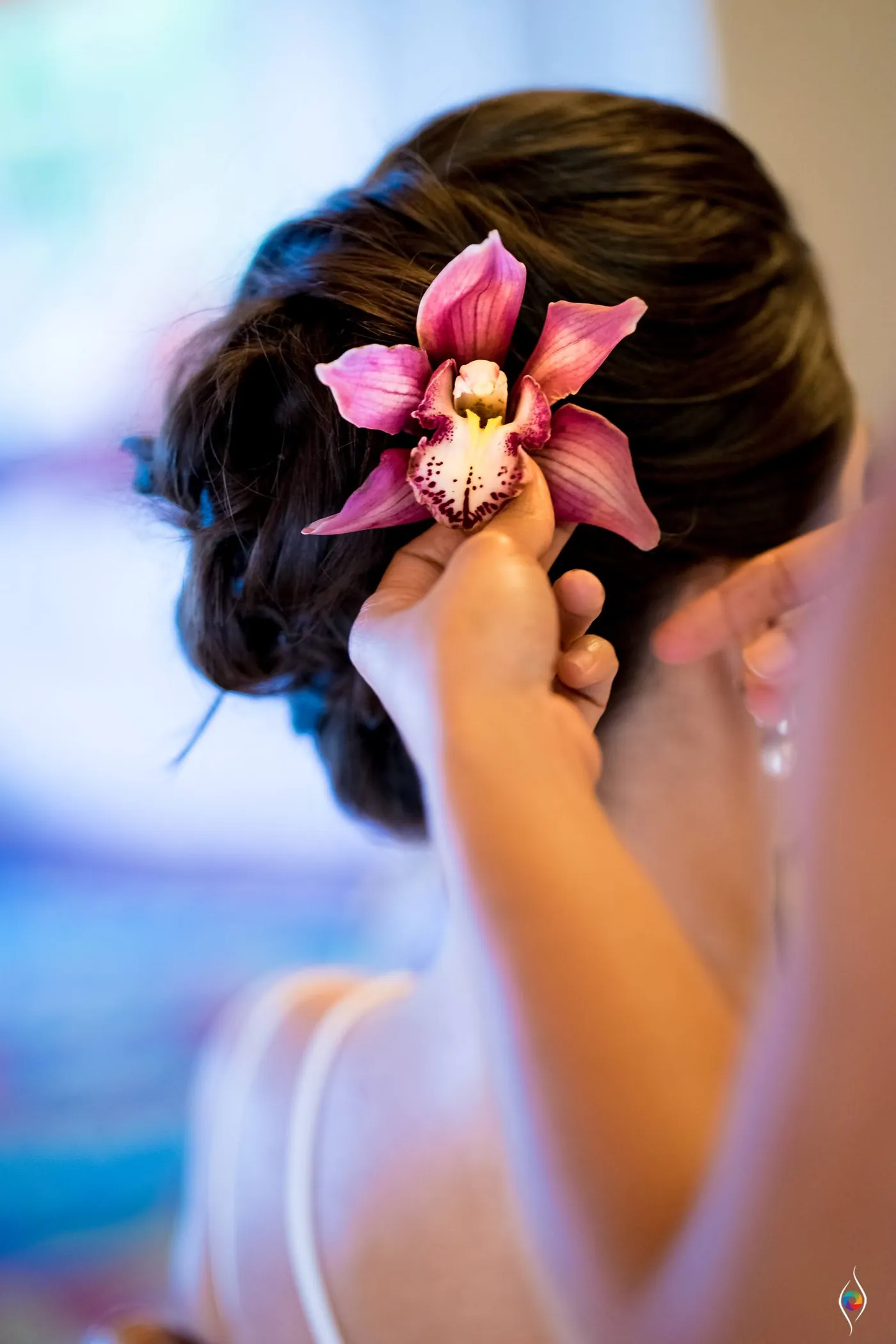 A pink orchid pinned into a dark updo, the sea a soft blur behind