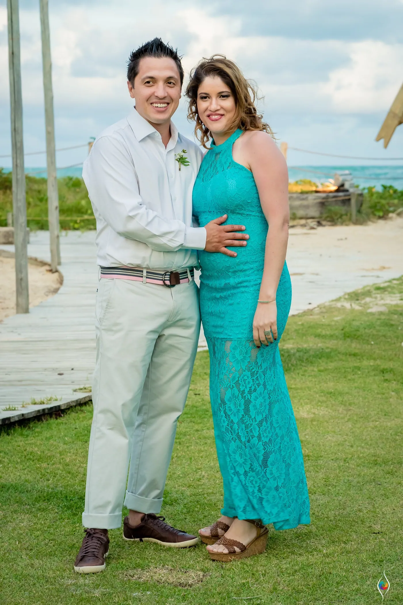 A man and a woman in teal lace stand close on the lawn, his hand on her waist